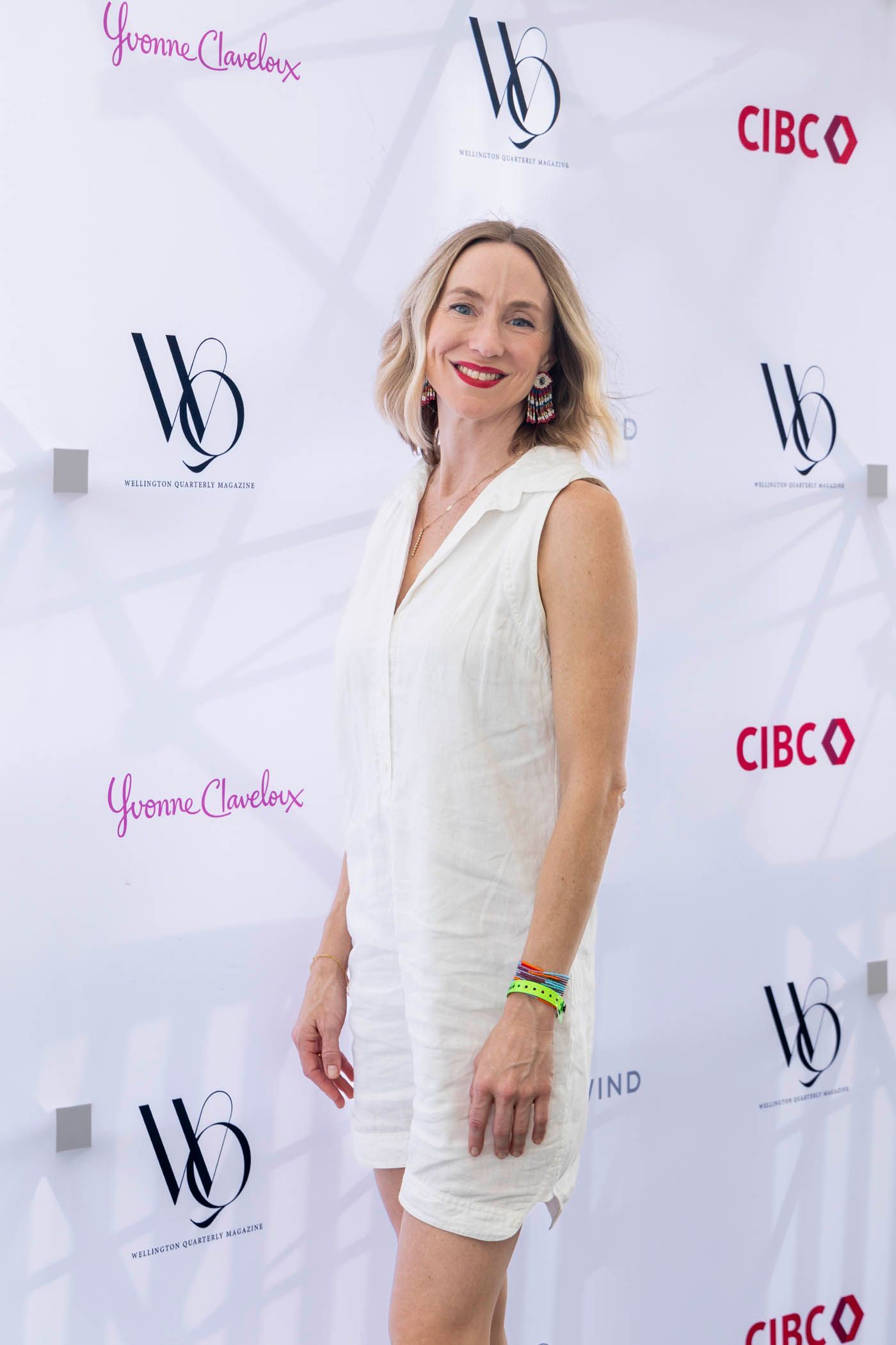A woman in a white dress is standing in front of a white wall.