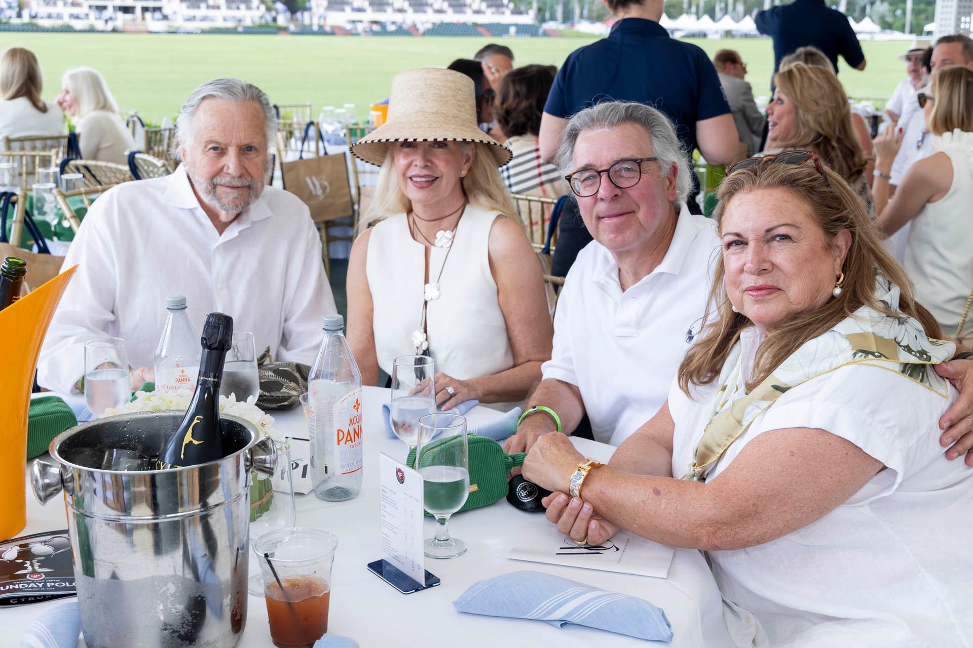 A group of people are sitting at a table with a bucket of champagne.