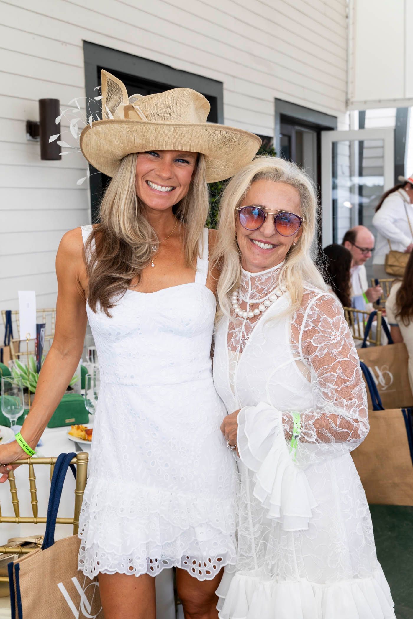 Two women in white dresses and hats are posing for a picture.