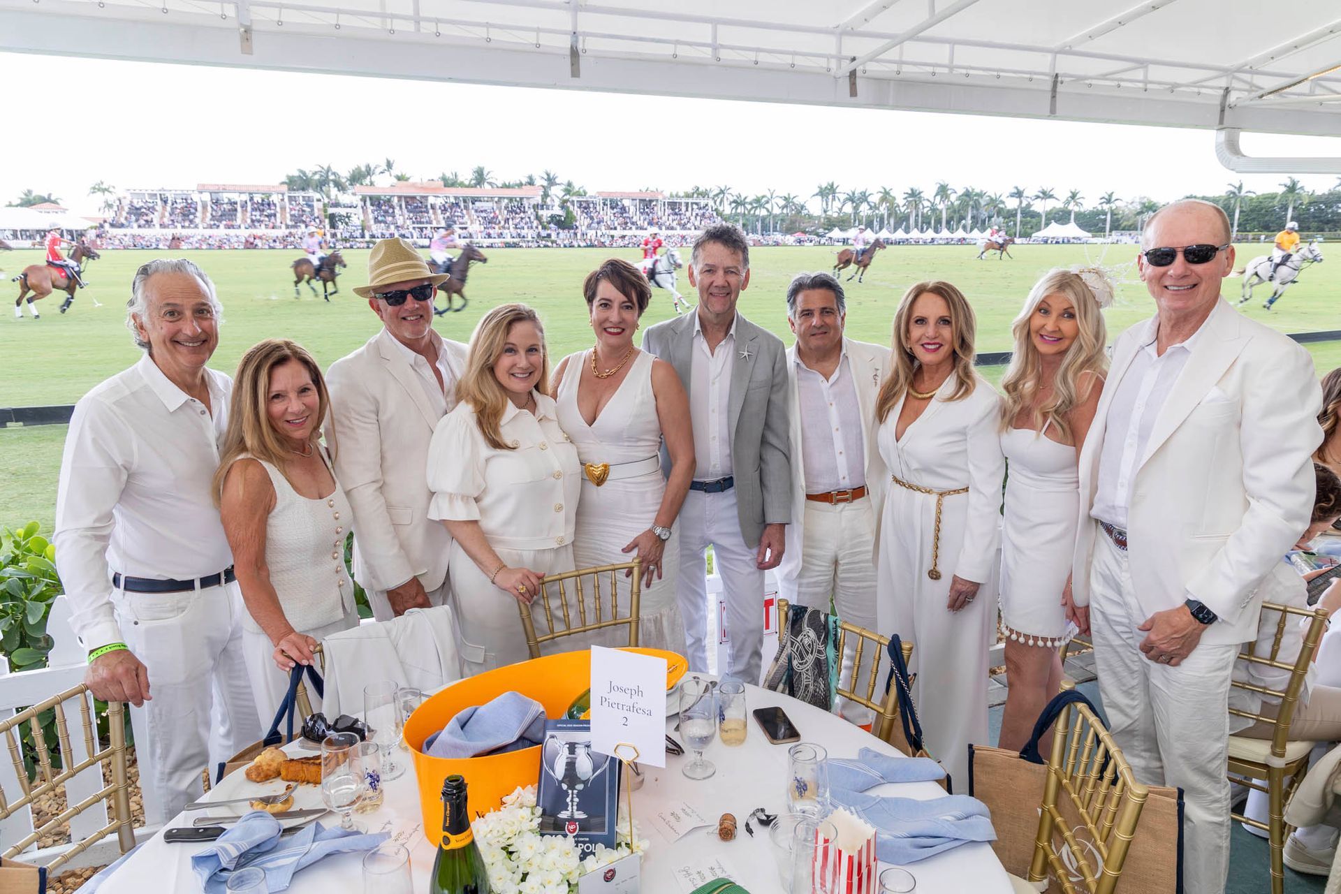 A group of people in white standing around a table at a polo match.