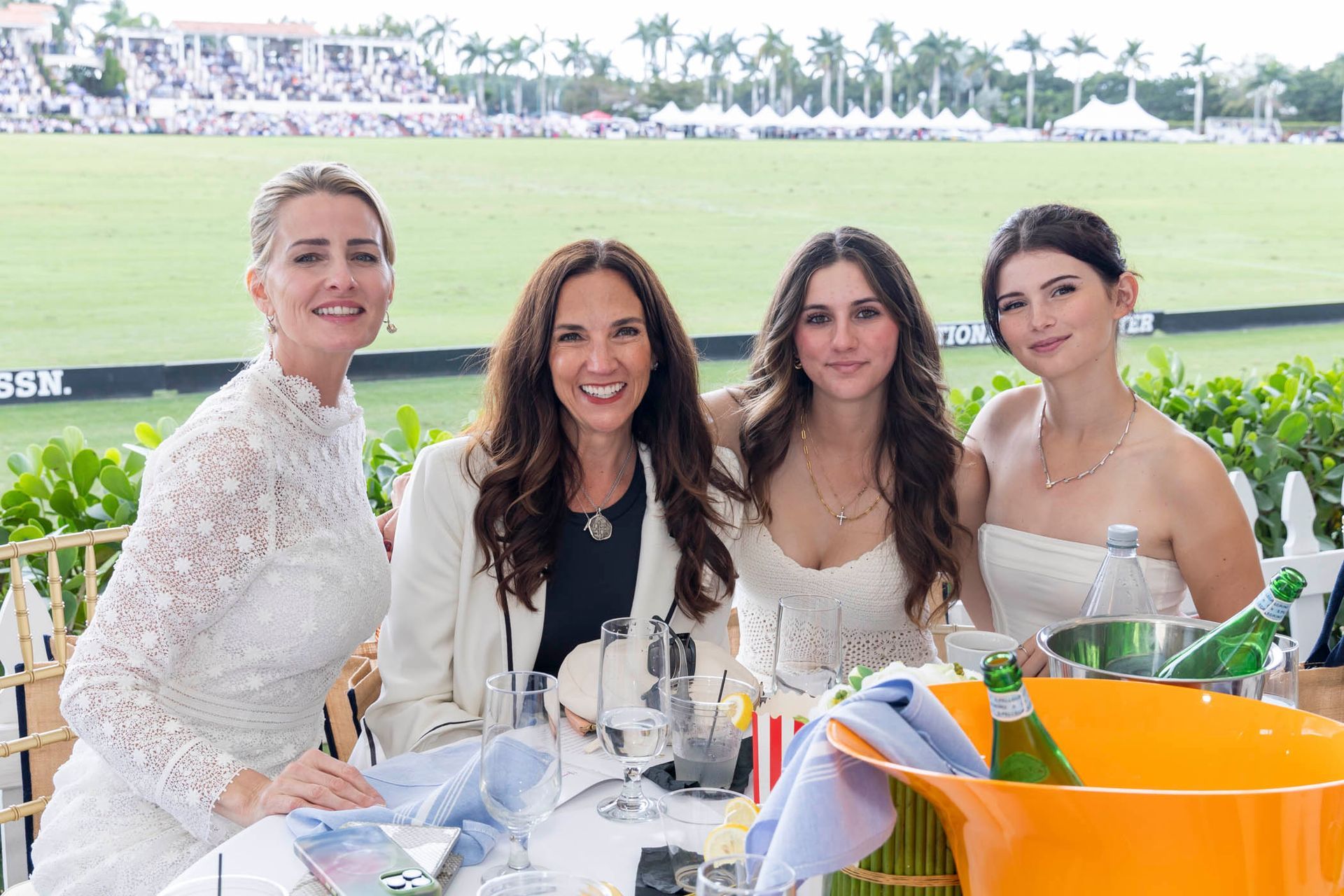 A group of women are sitting at a table with a bucket of champagne.