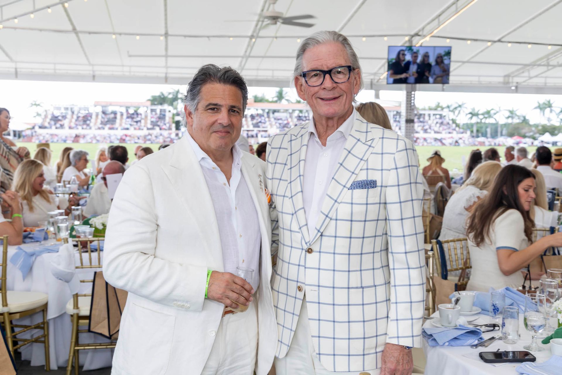 Two men in white suits are posing for a picture in a tent.