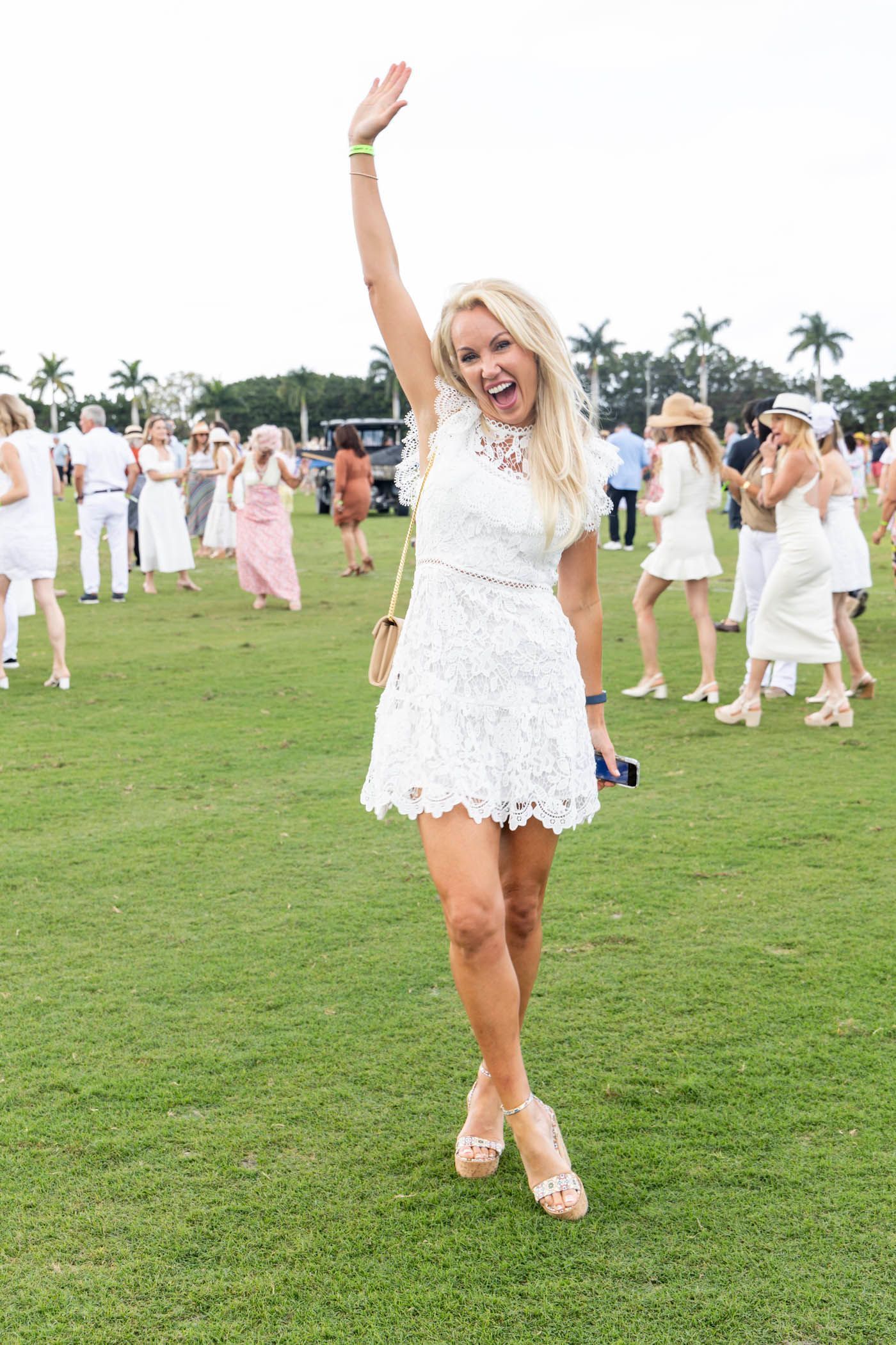 A woman in a white dress is standing in a field with her hand in the air.