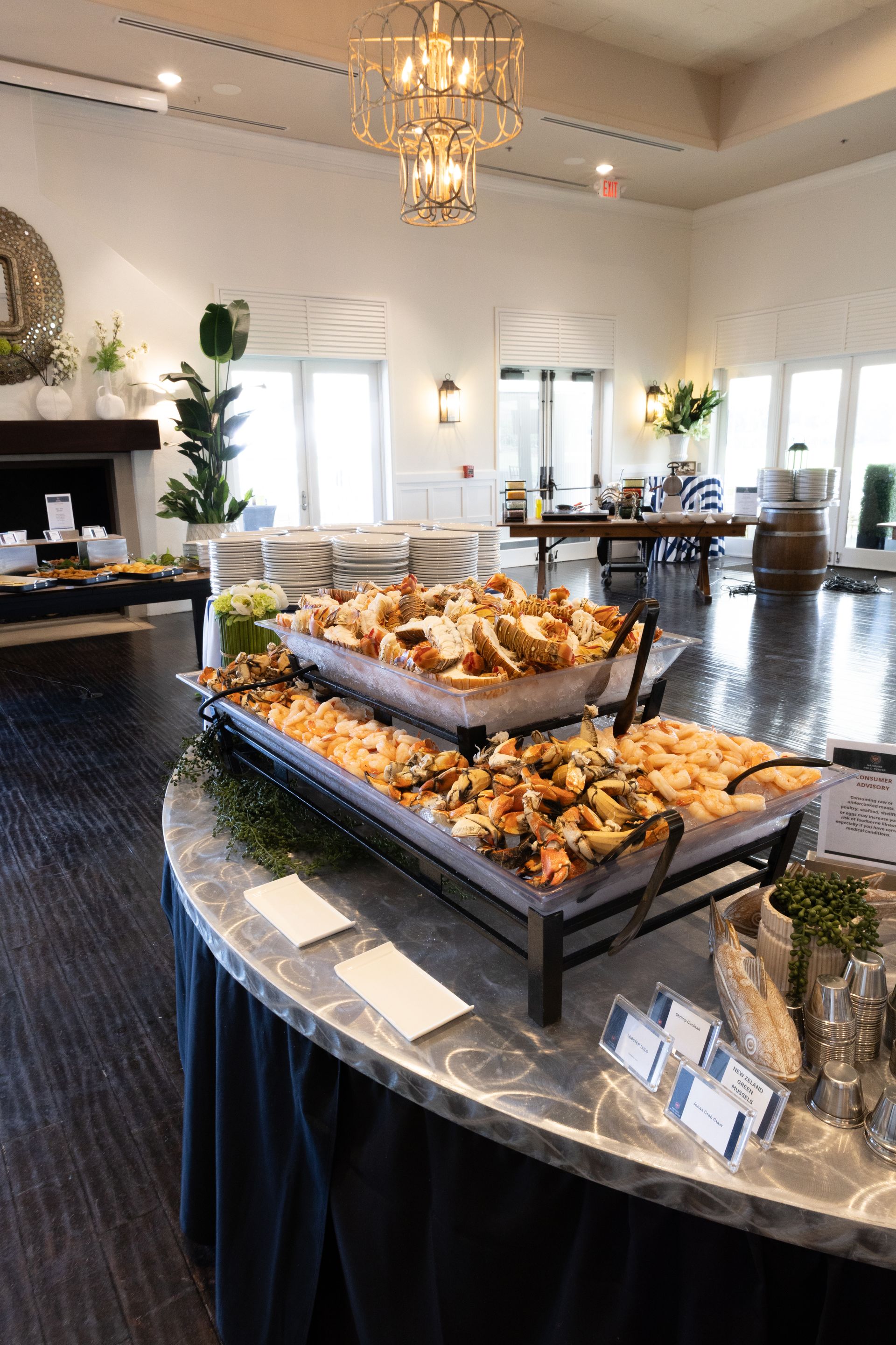 Buffet table with trays of food in a bright, open room. White walls, dark wood floor, chandelier.
