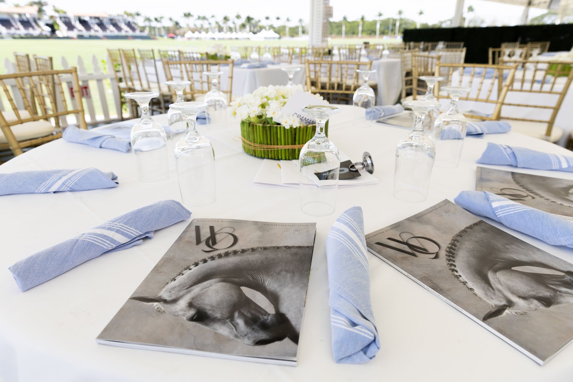 Round table set for a formal event, with white linens, blue napkins, and place settings.
