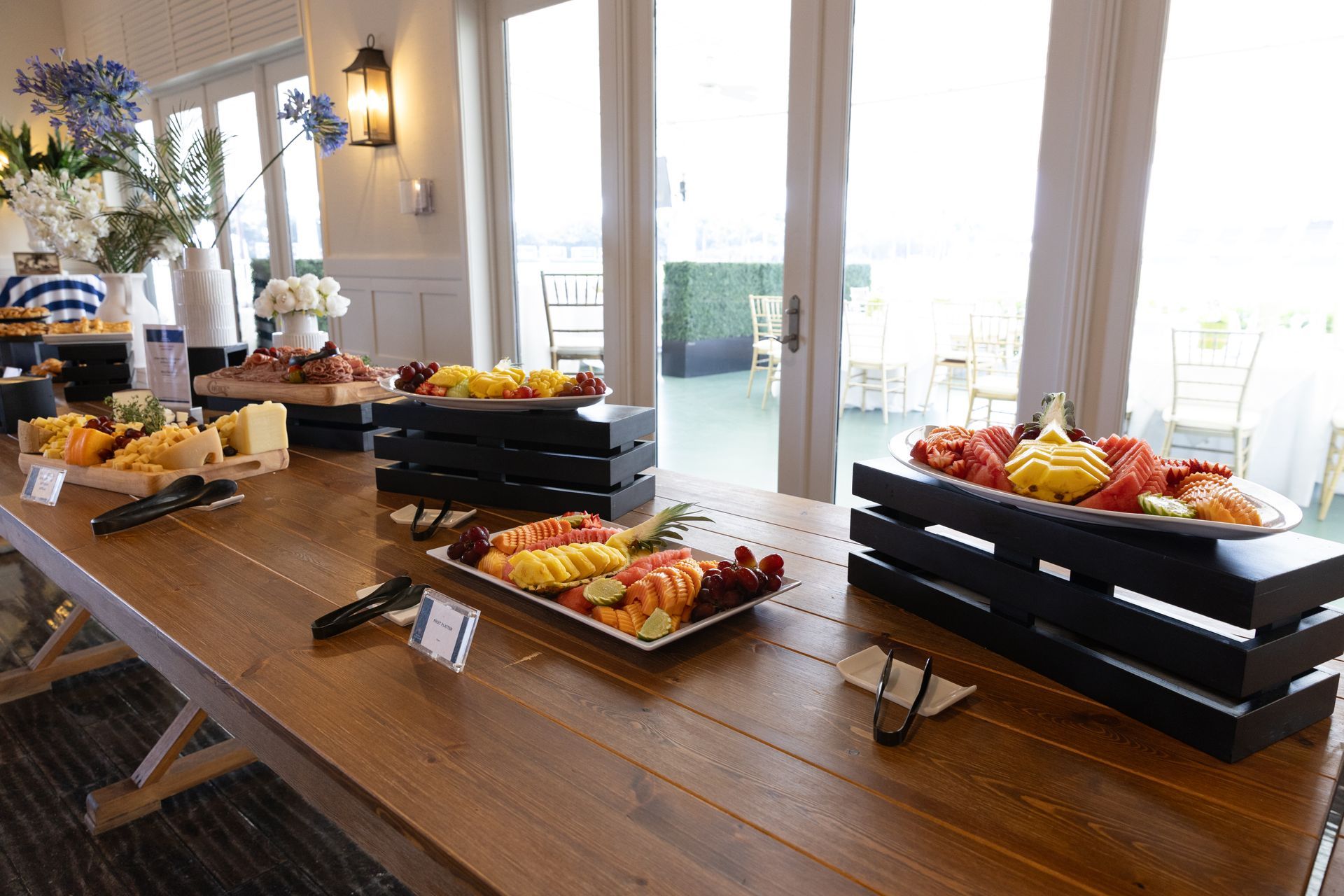 Buffet table with fruit, cheese, and appetizers, set outdoors with an ocean view.