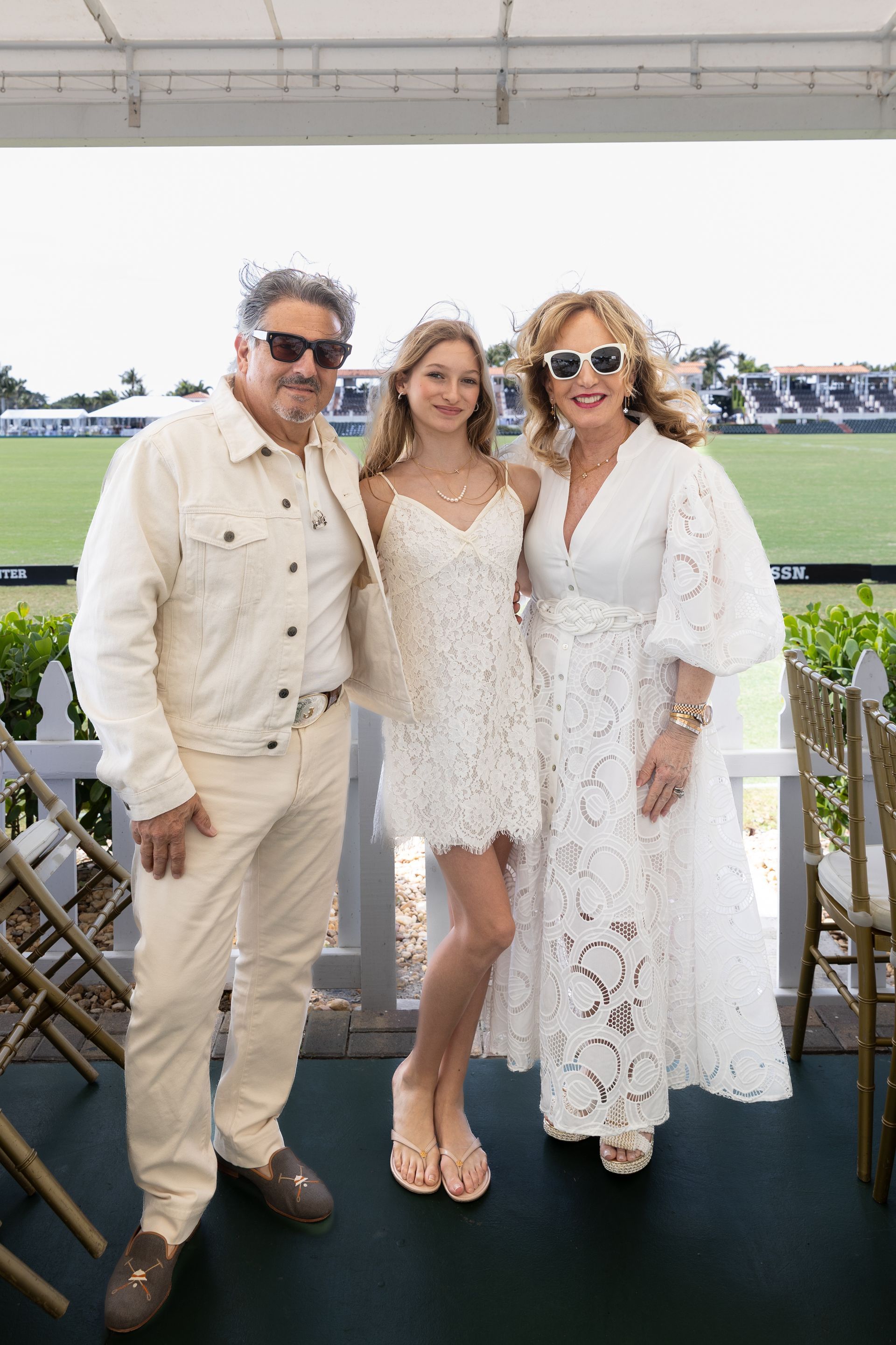 Family poses outdoors. Man in cream outfit, young person in white dress, woman in white dress.