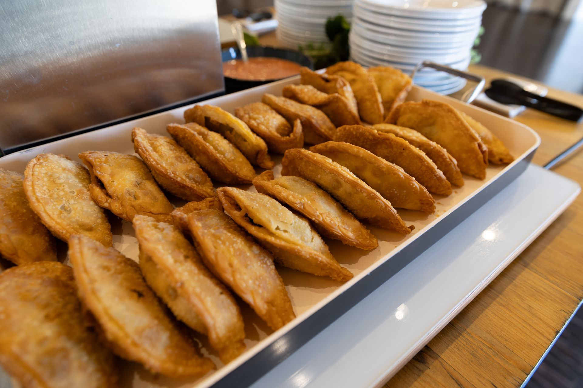 Tray of golden-brown, fried pastries, possibly empanadas, on a buffet table.