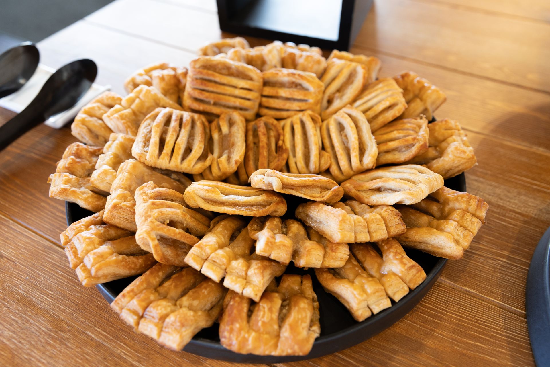 Arrangement of square pastries on a black plate, set on a wooden surface.