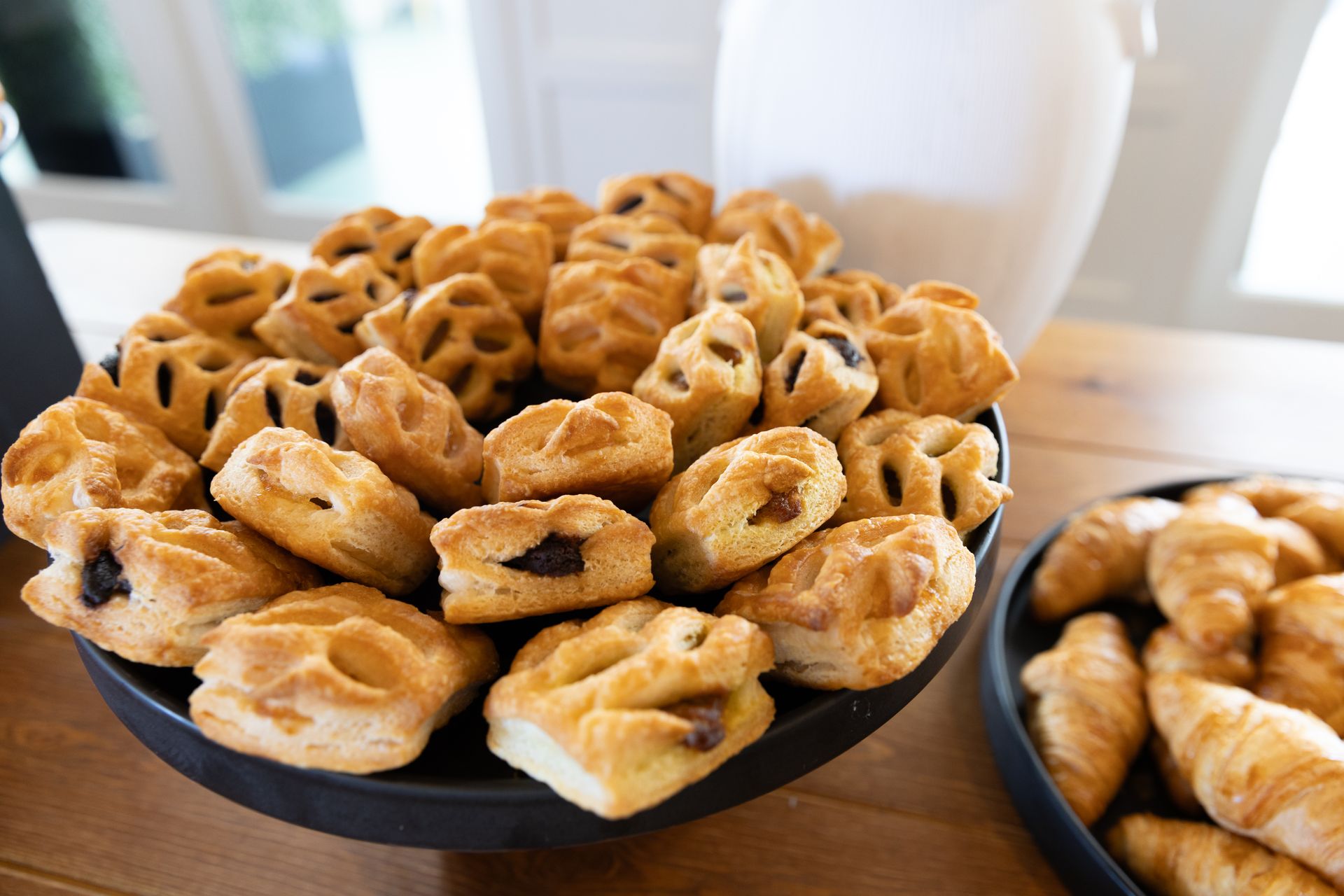 Close-up of pastries in a black bowl, next to mini croissants on a wooden table.