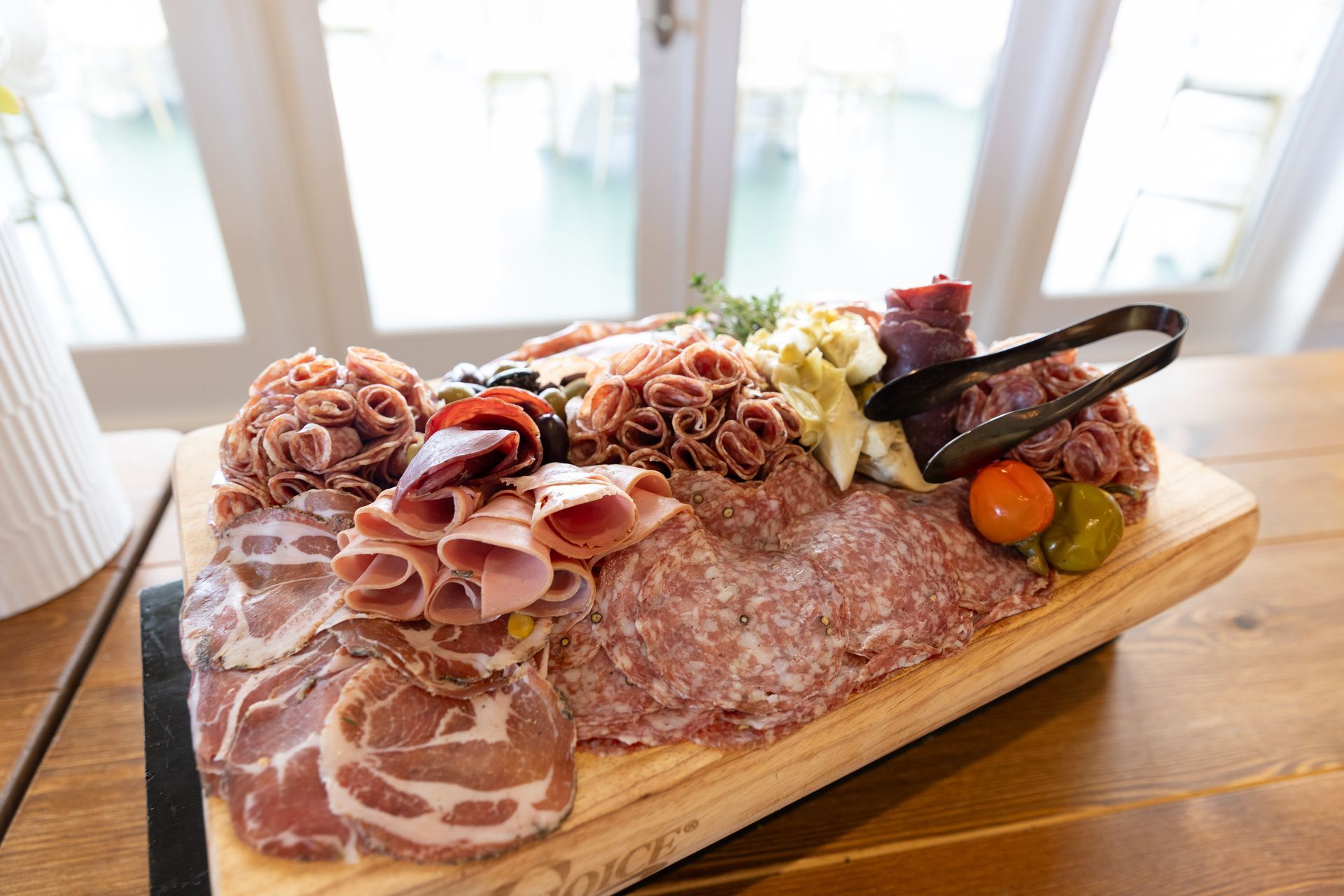 Charcuterie board with various meats, olives, artichokes, and a cherry tomato on a wooden surface.