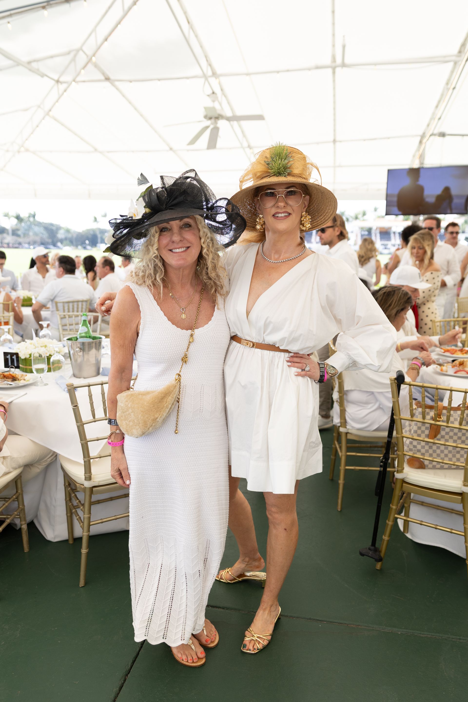 Two women in white outfits and hats pose together outdoors.