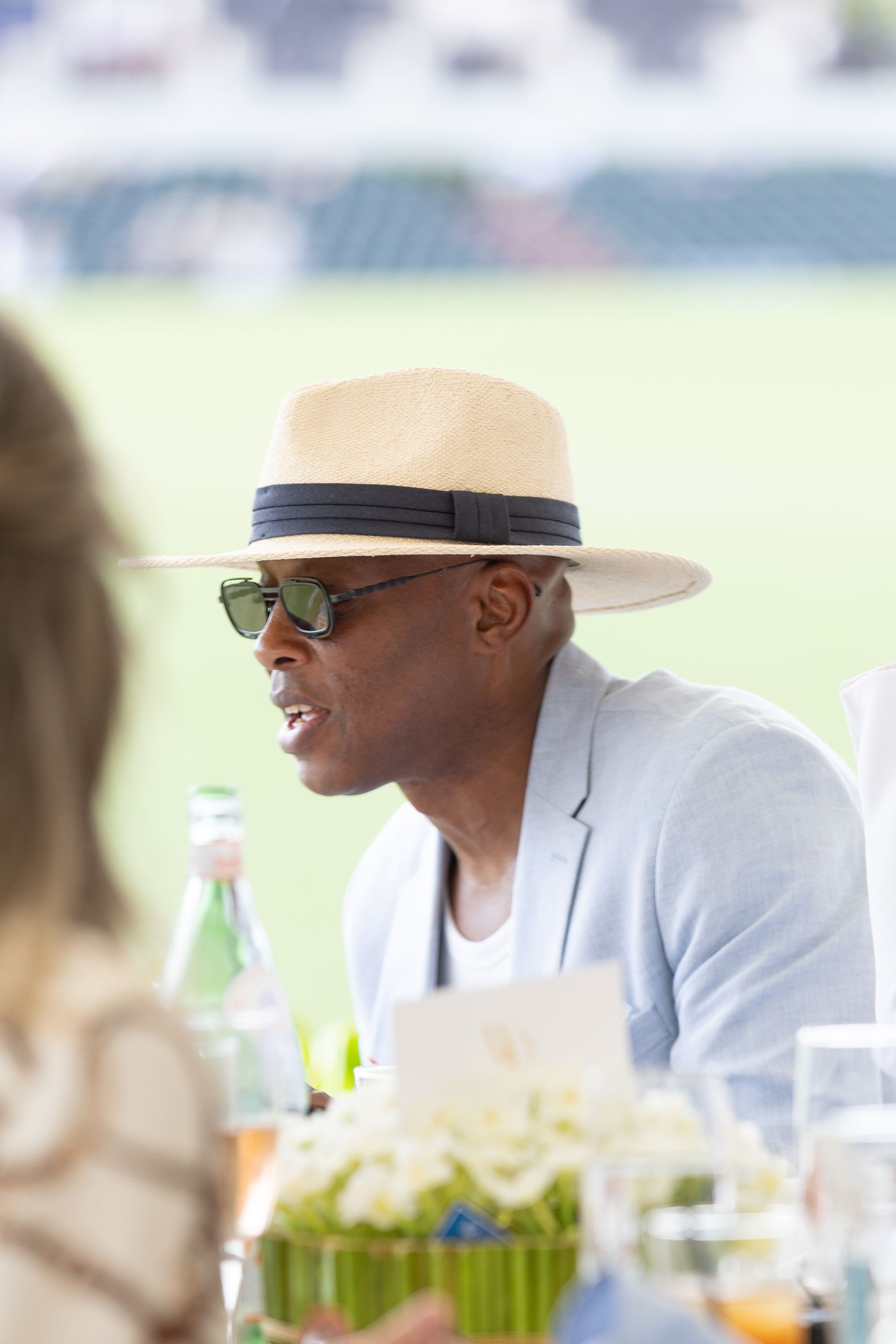 Man wearing a straw hat and sunglasses at an outdoor event, looking to his right.