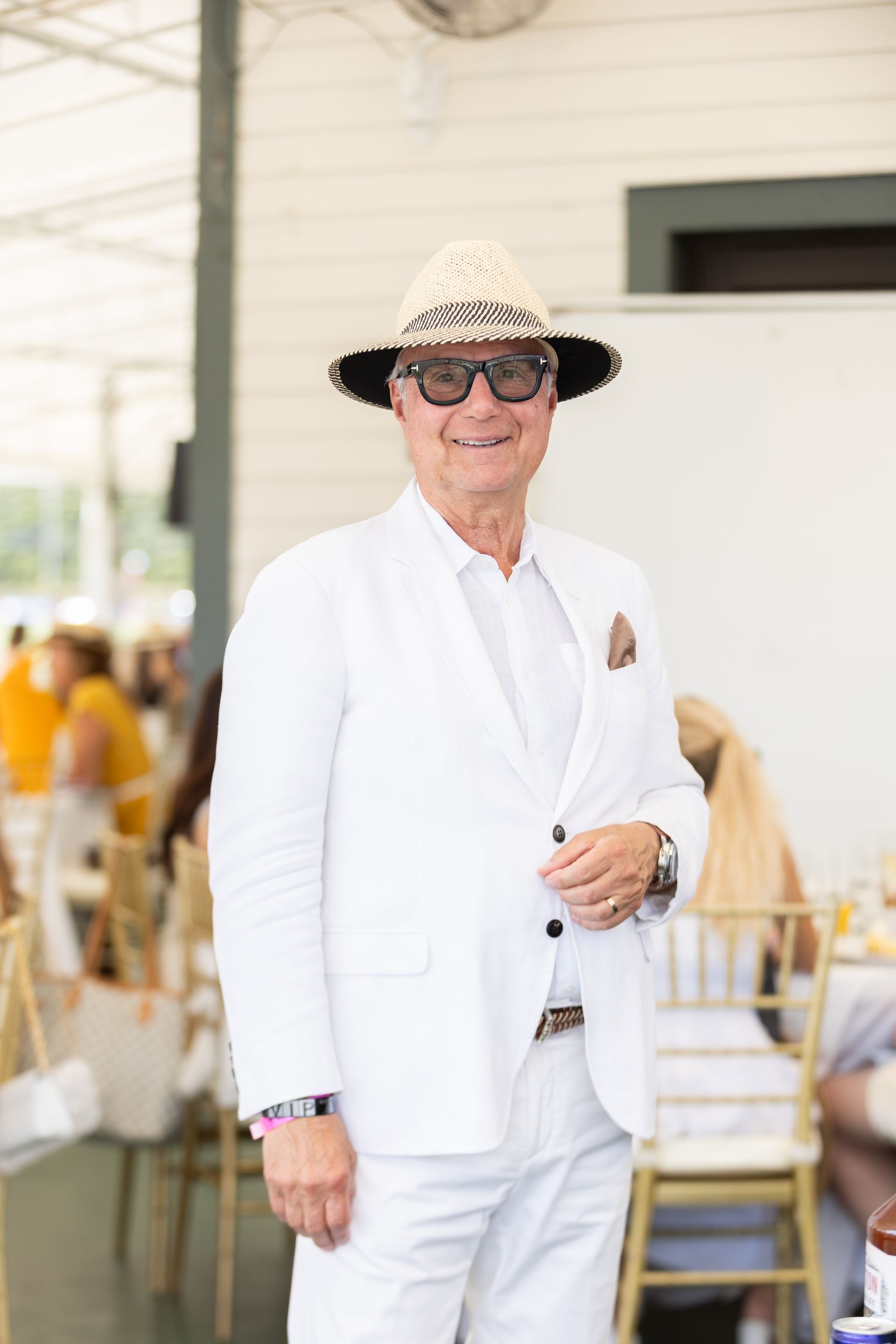 Man in white suit and straw hat smiles, stands outdoors.