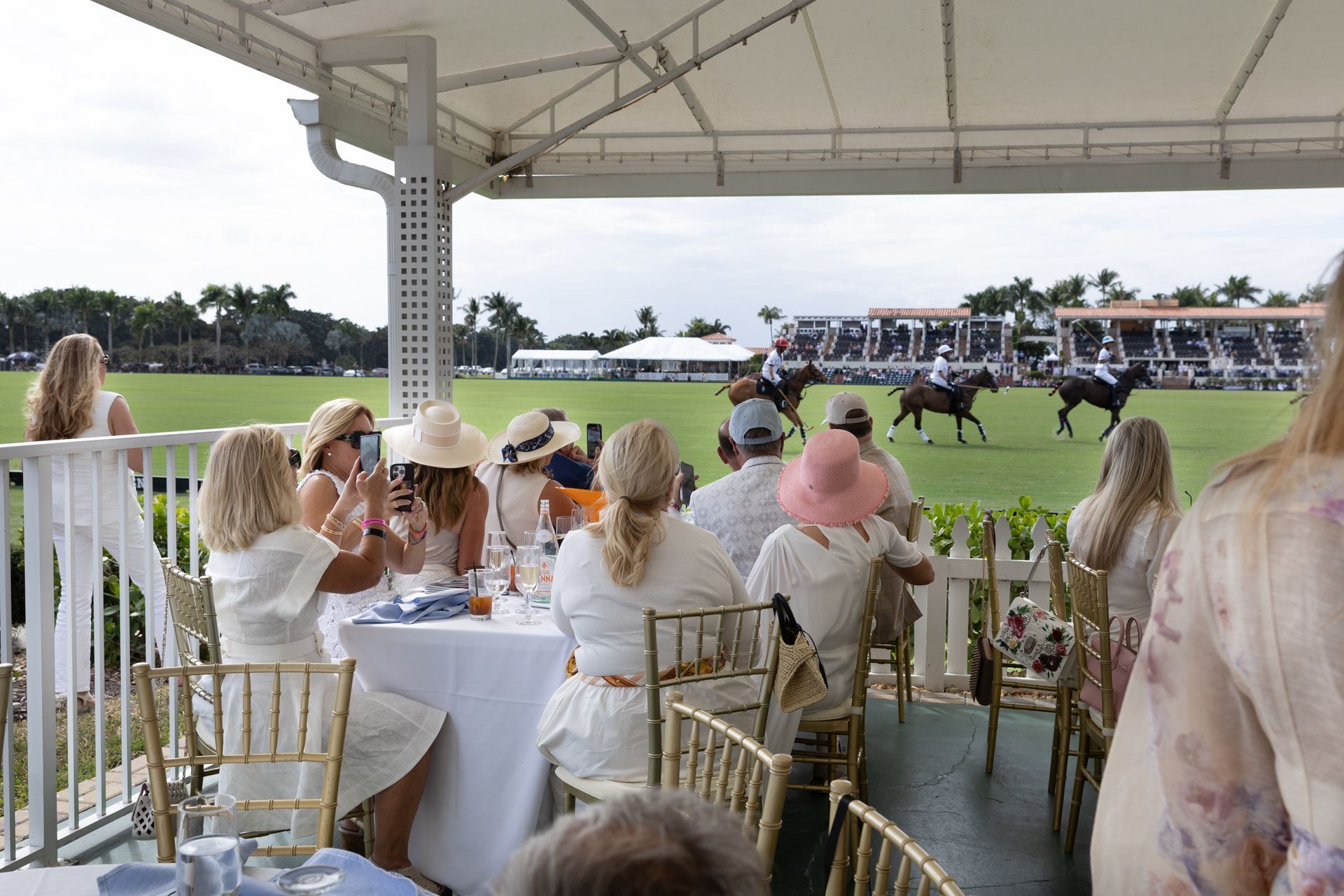 People watching a polo match from a covered outdoor seating area.