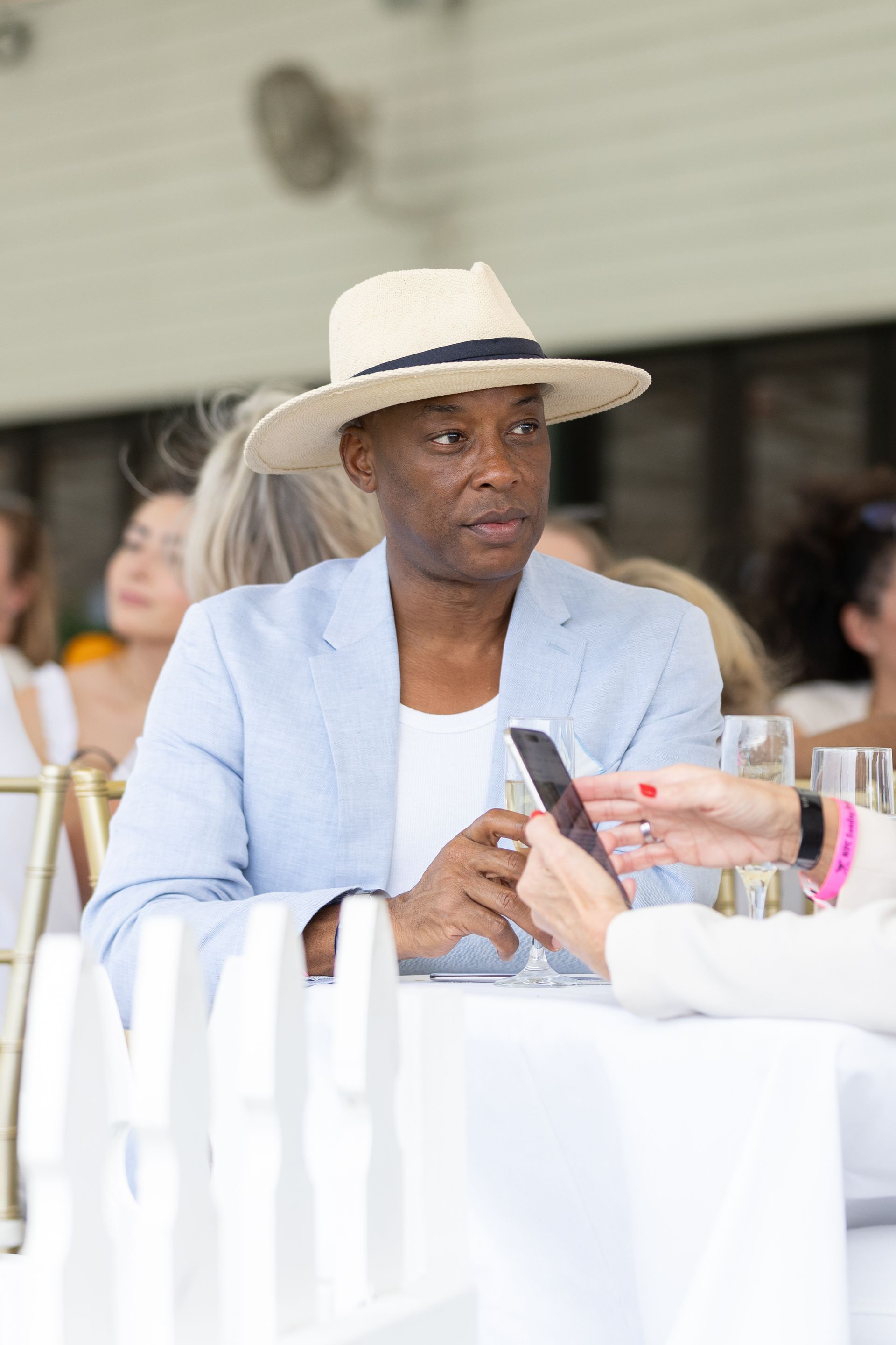 Man in a light blue blazer and straw hat, seated at a white table.