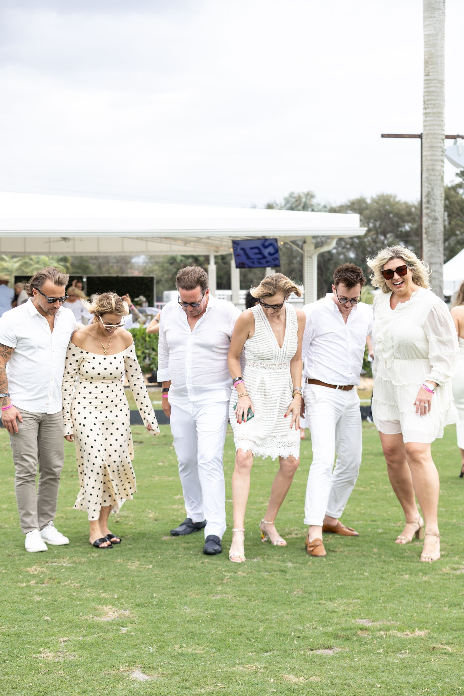 Group of people in white attire on grass, some are dancing.
