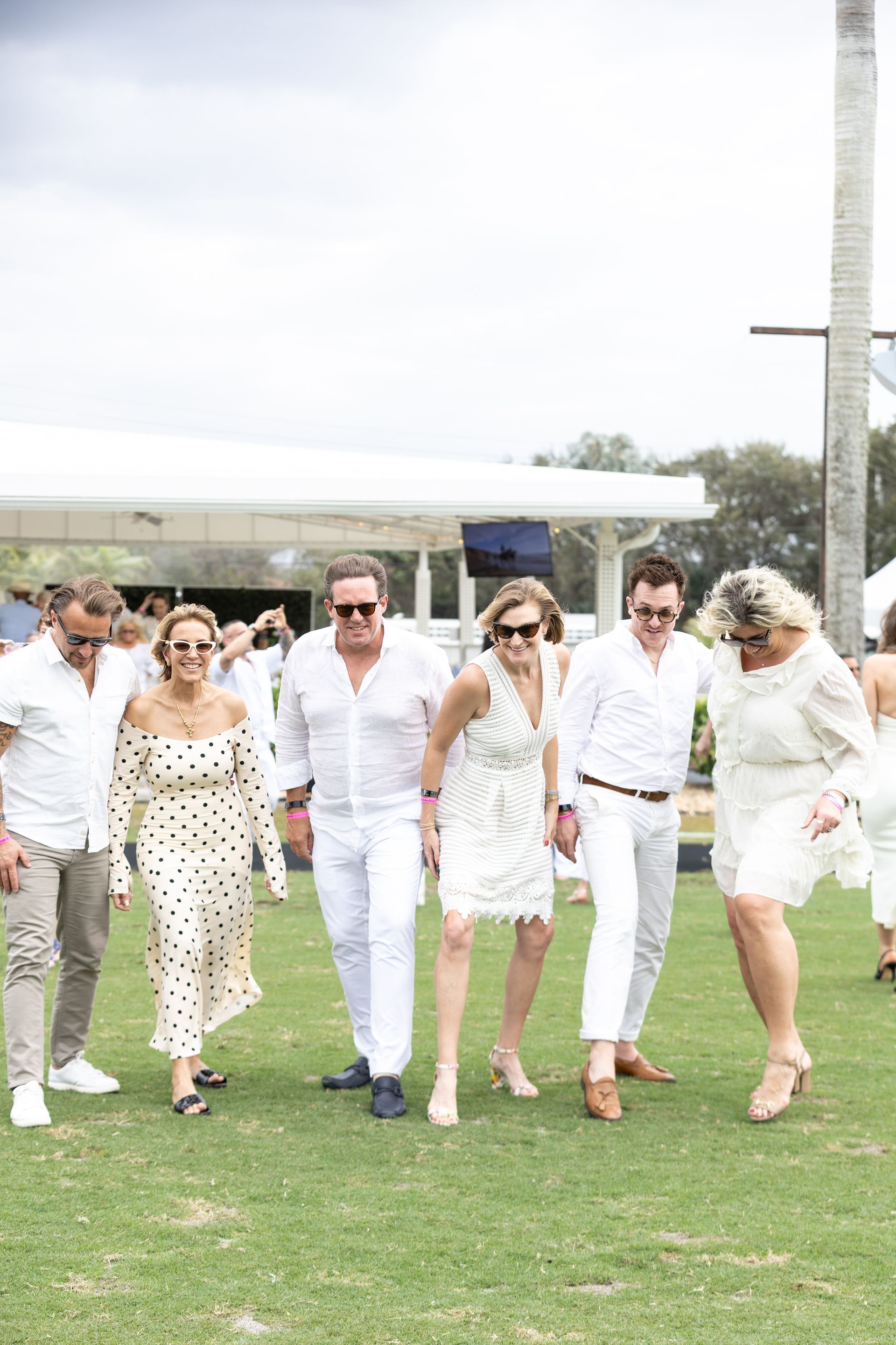 Group of people in white outfits walking on grass.