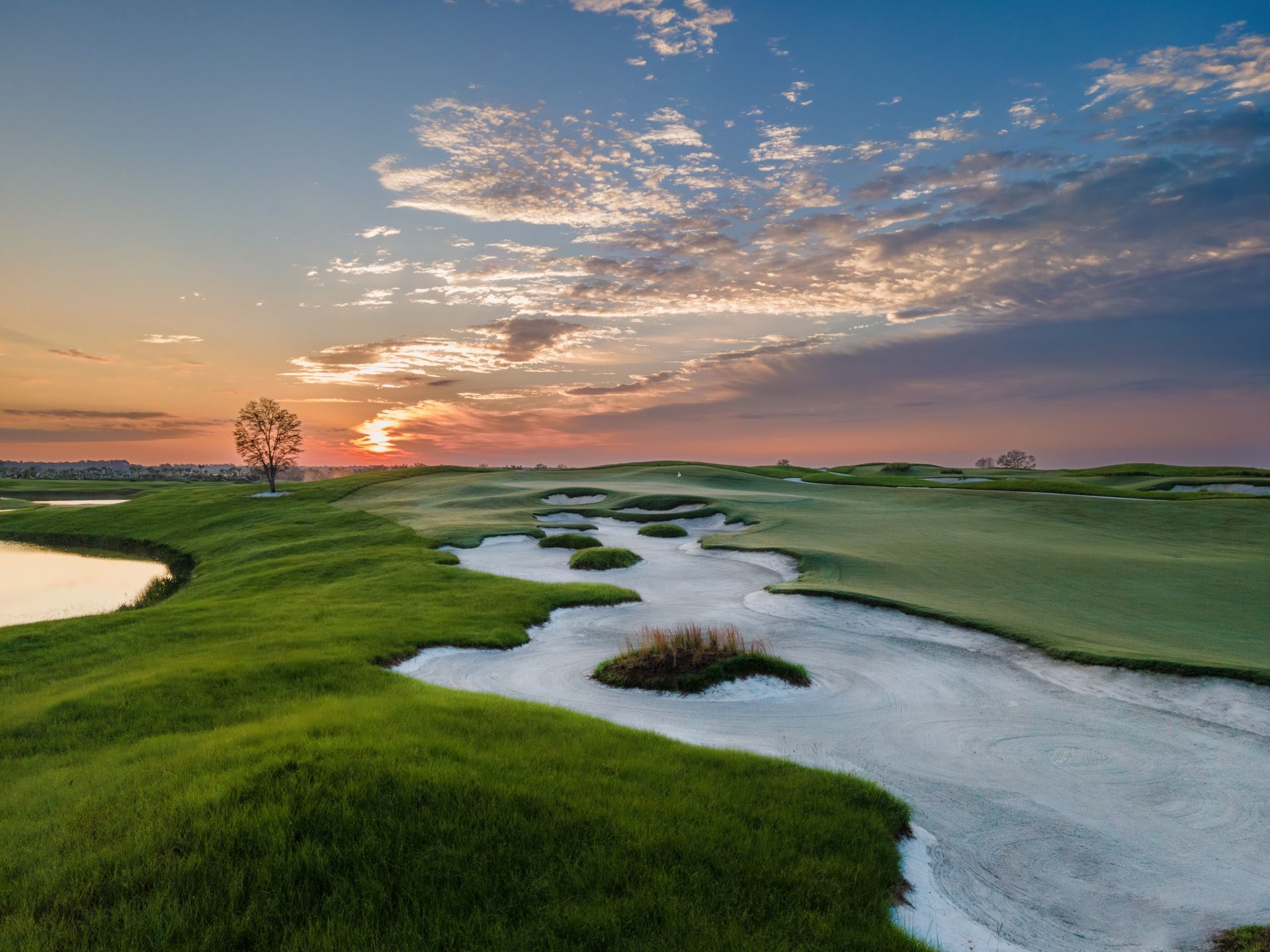 a golf course with a river running through it and a sunset in the background