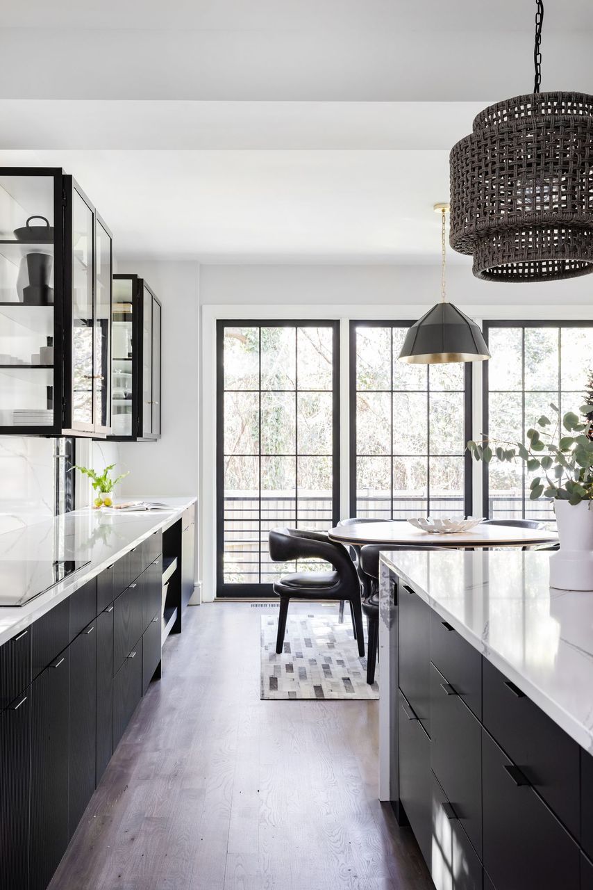 A Kitchen With Black Cabinets, White Counter Tops, A Table And Chairs