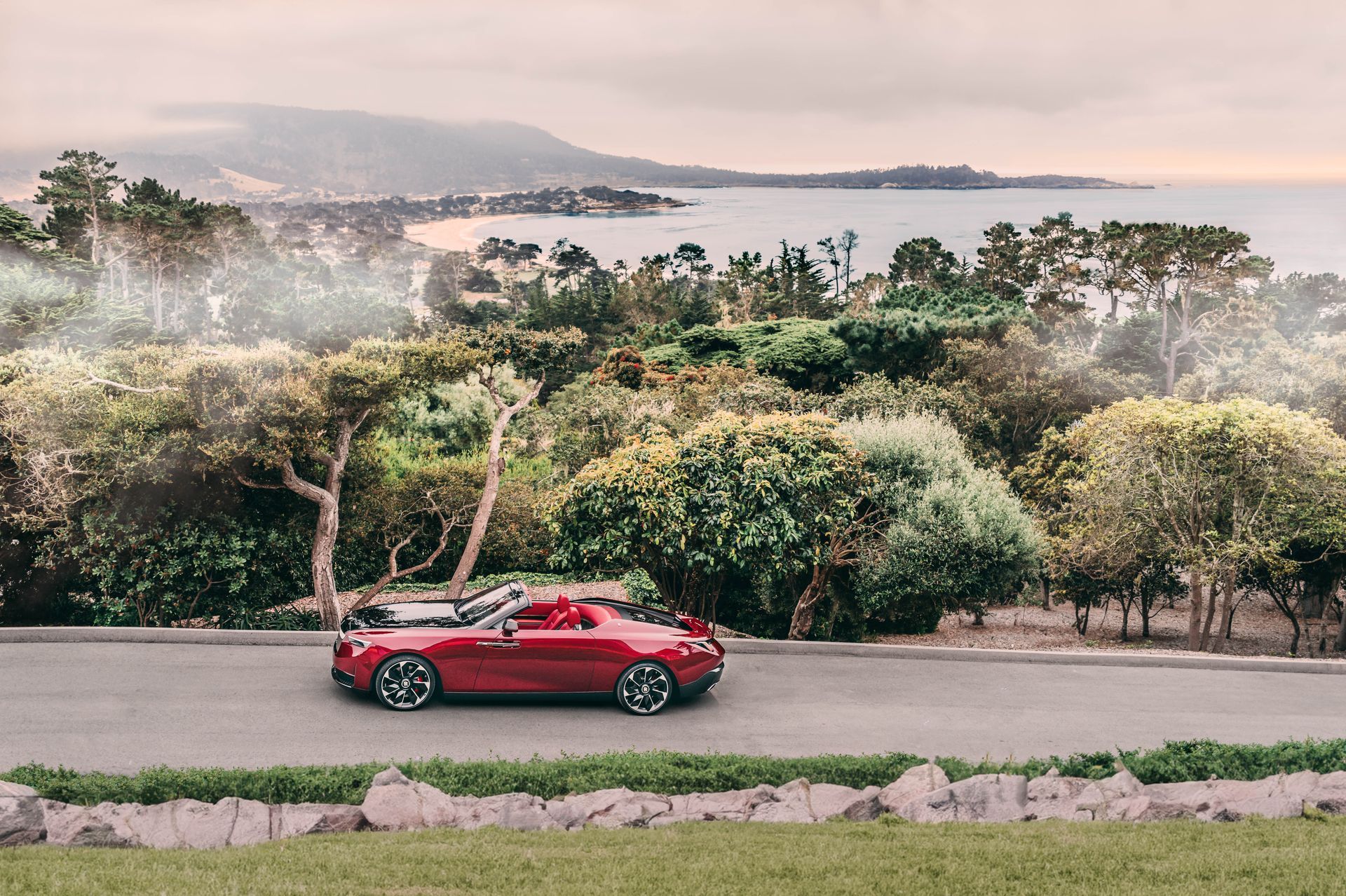A Red Car Is Driving Down A Road Next To A Body Of Water