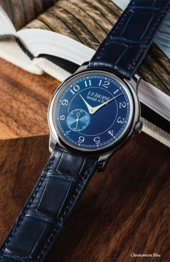 A blue watch is sitting on a wooden table next to a book.