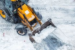 A yellow tractor plowing snow on a road, captured from a high-angle perspective.