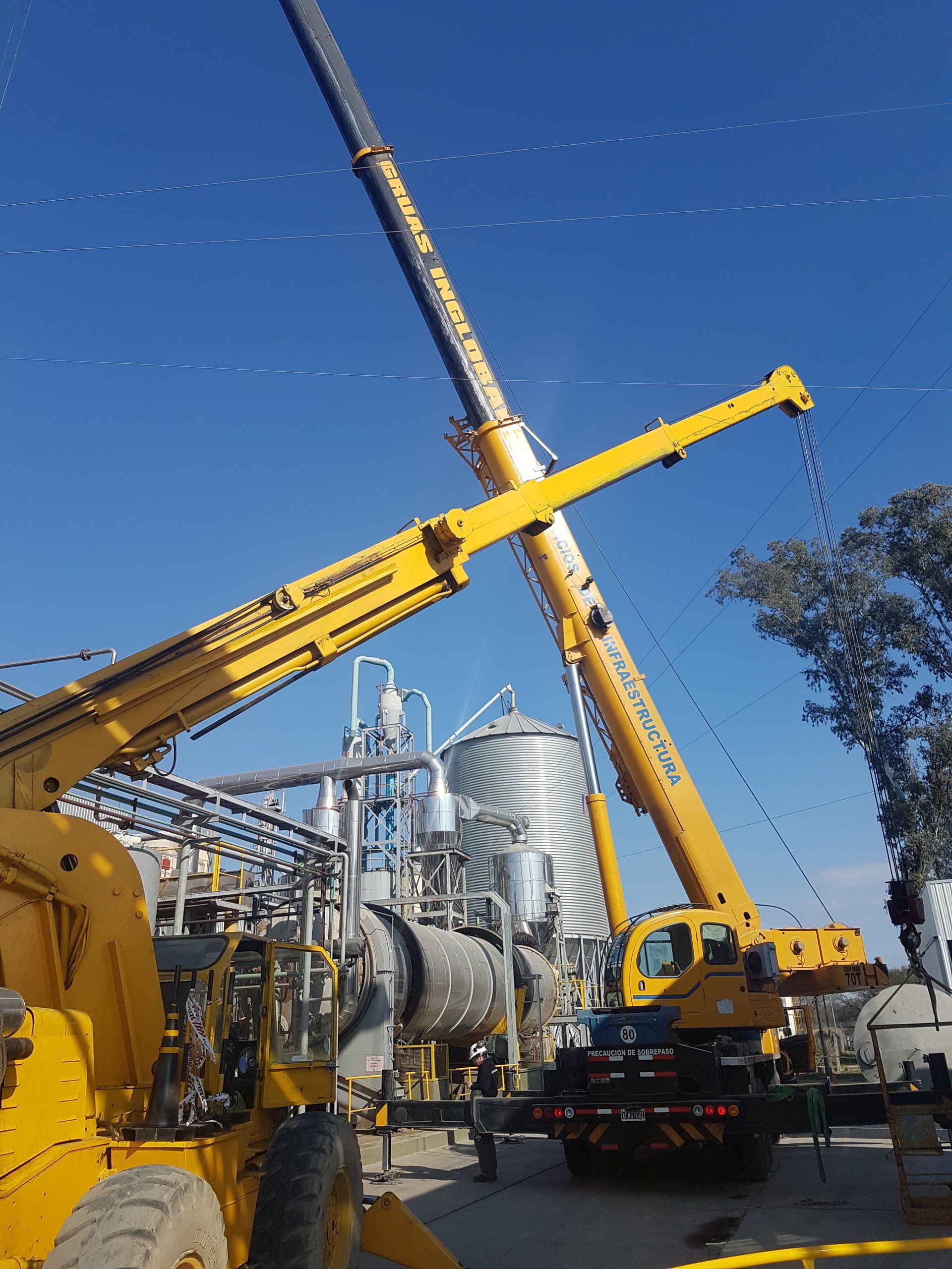 Una gran grúa amarilla está parada frente a una fábrica. - Grúas Inglobal SRL
