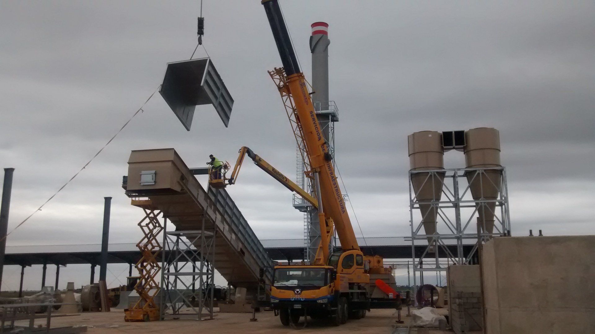 Una grúa está levantando una gran pieza de metal en un sitio de construcción. - Grúas Inglobal SRL