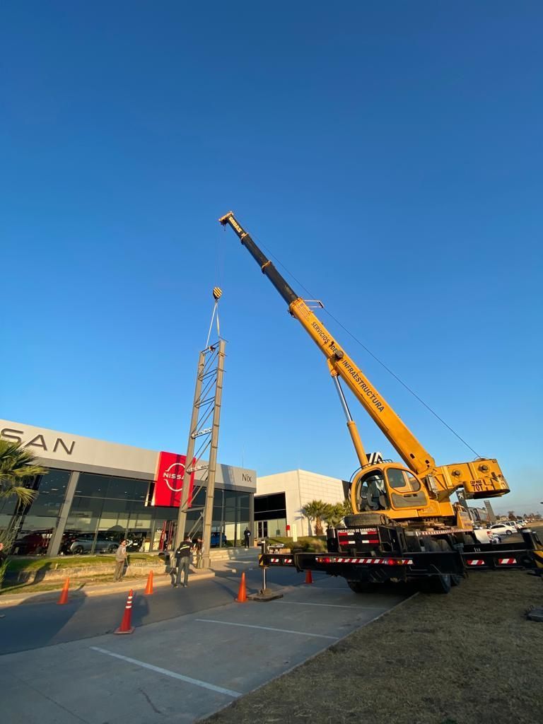 Una gran grúa amarilla está levantando una estructura frente a un concesionario Nissan.