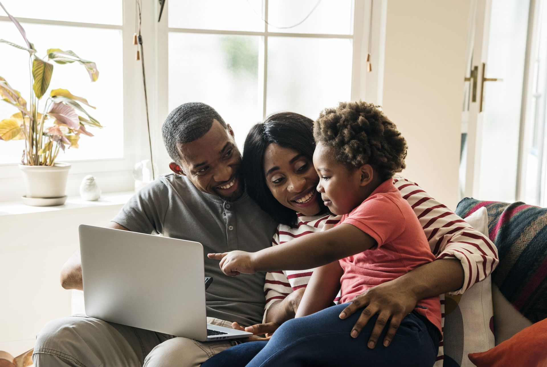 a family is sitting on a couch looking at a laptop computer .