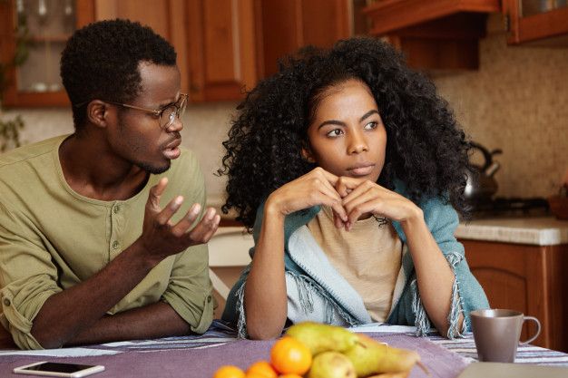 um homem e uma mulher estão sentados à mesa de uma cozinha discutindo.