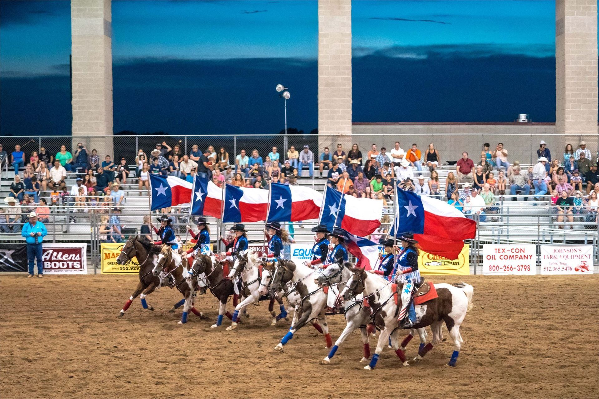 A group of people riding horses carrying a texas flag at the Taylor Rodeo