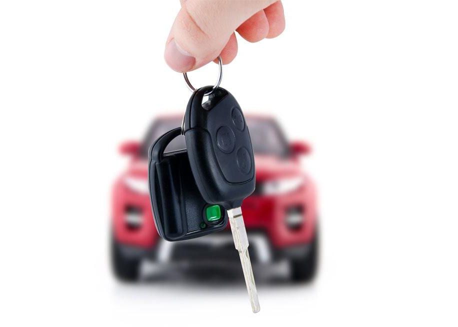 Una persona sostiene la llave de un auto frente a un auto rojo.