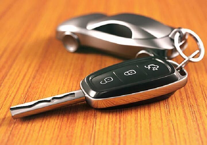 Una llave de auto está sobre una mesa de madera al lado de un auto de juguete.