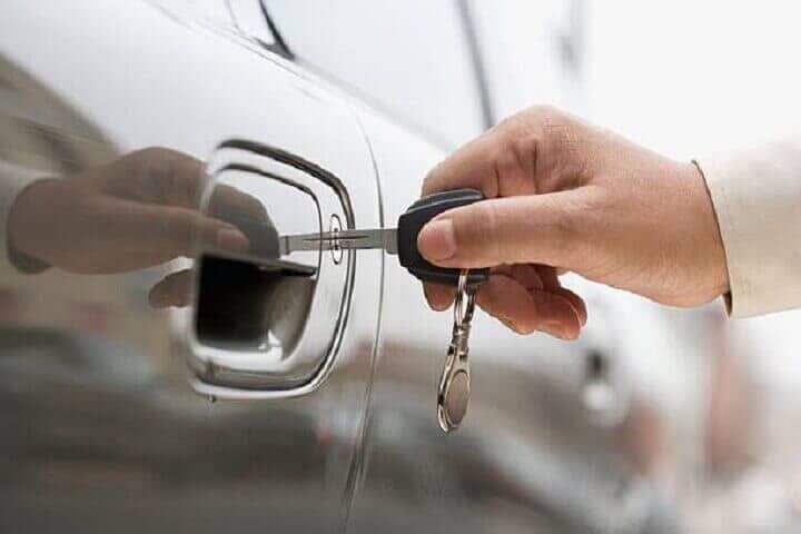 Una persona sostiene la llave de un auto frente a la puerta de un auto.