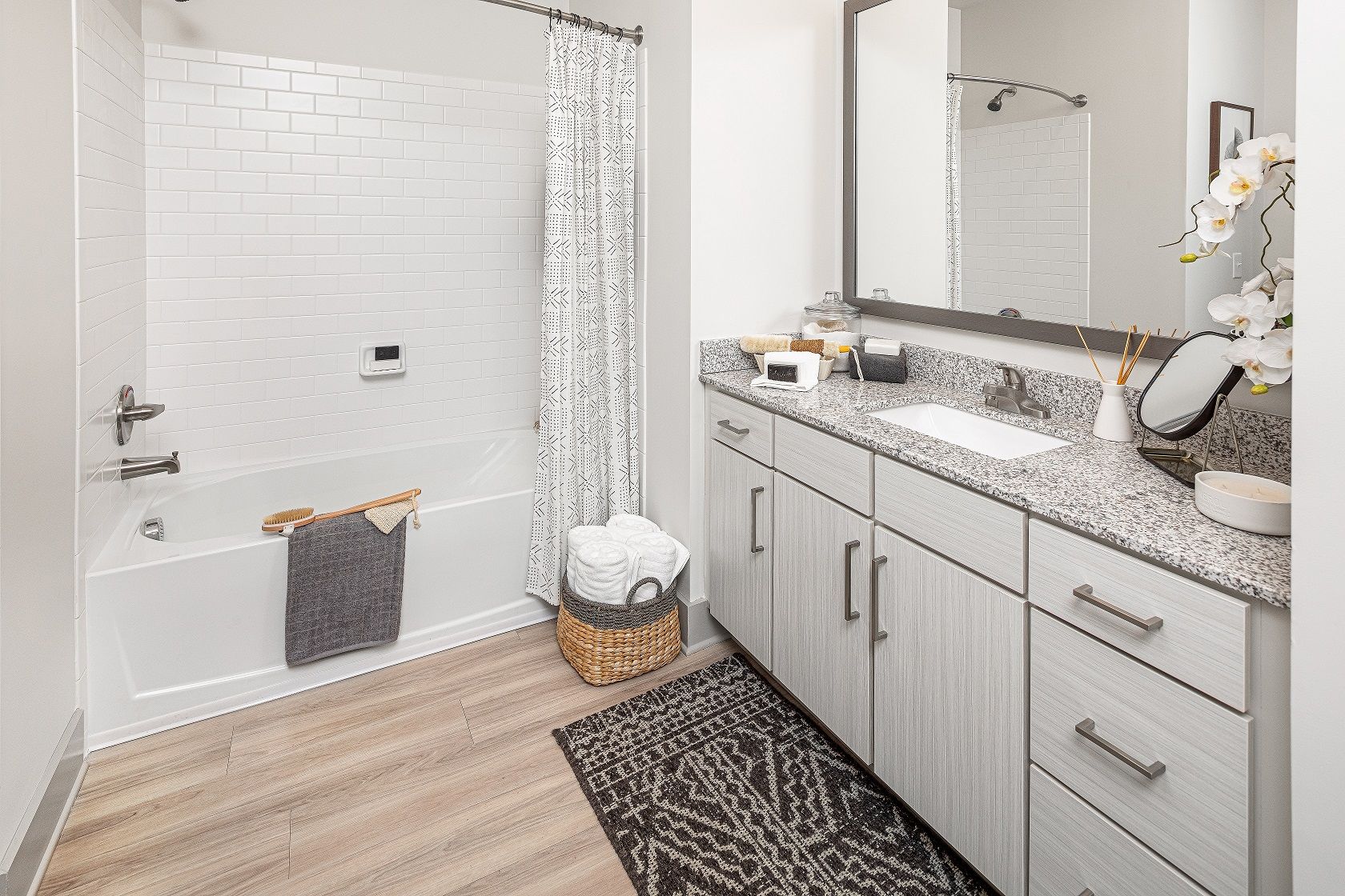 A bathroom with a bathtub , sink , mirror and rug.