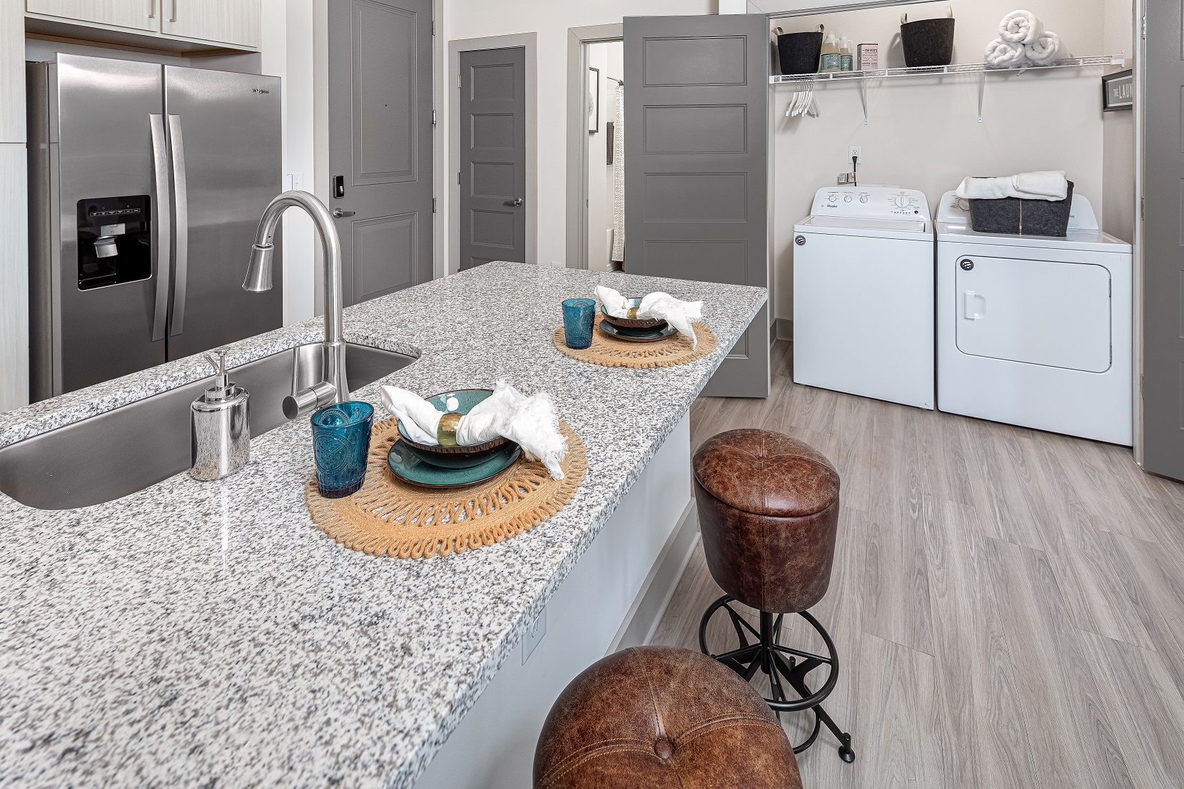 A kitchen with granite counter tops , a sink , a refrigerator , and a laundry room.