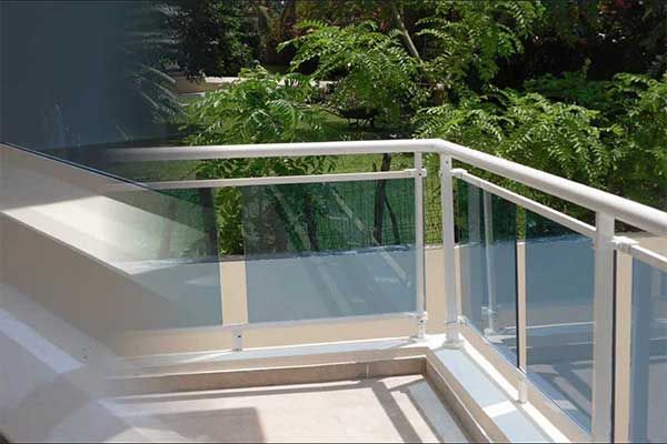 Un balcón con barandilla de cristal y árboles al fondo