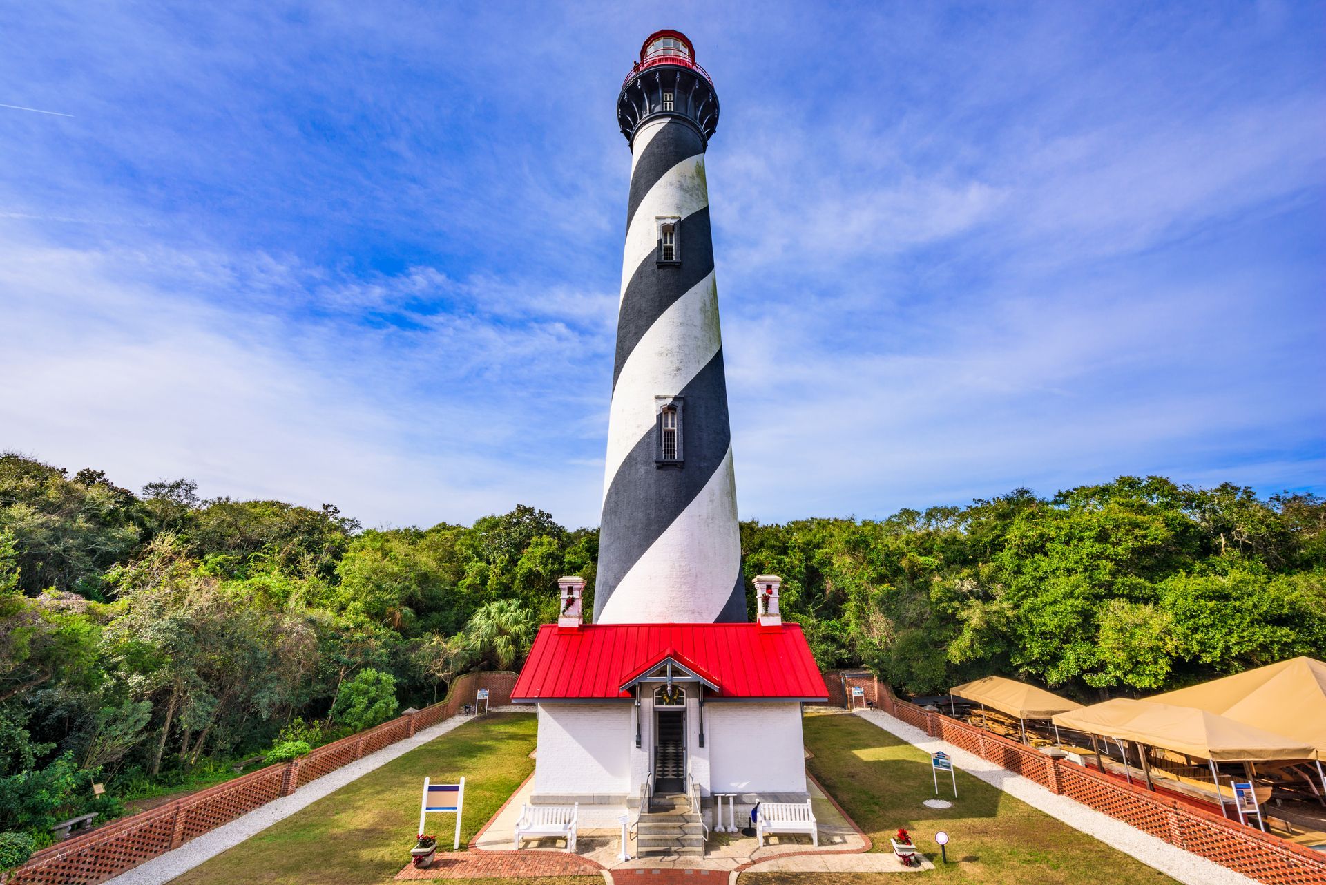 A black and white lighthouse with a red roof is surrounded by trees.