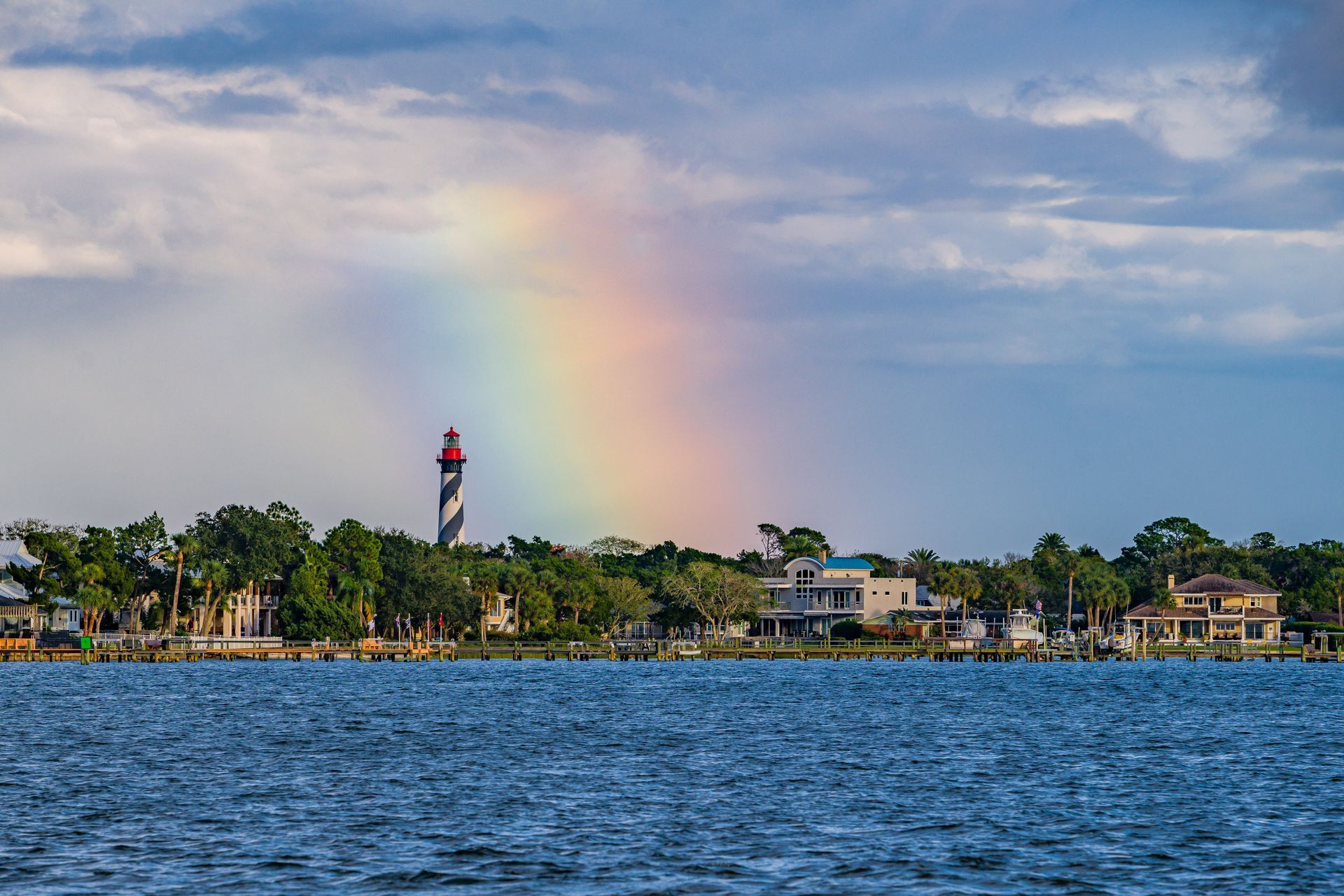 A rainbow is visible over a body of water with a lighthouse in the background.