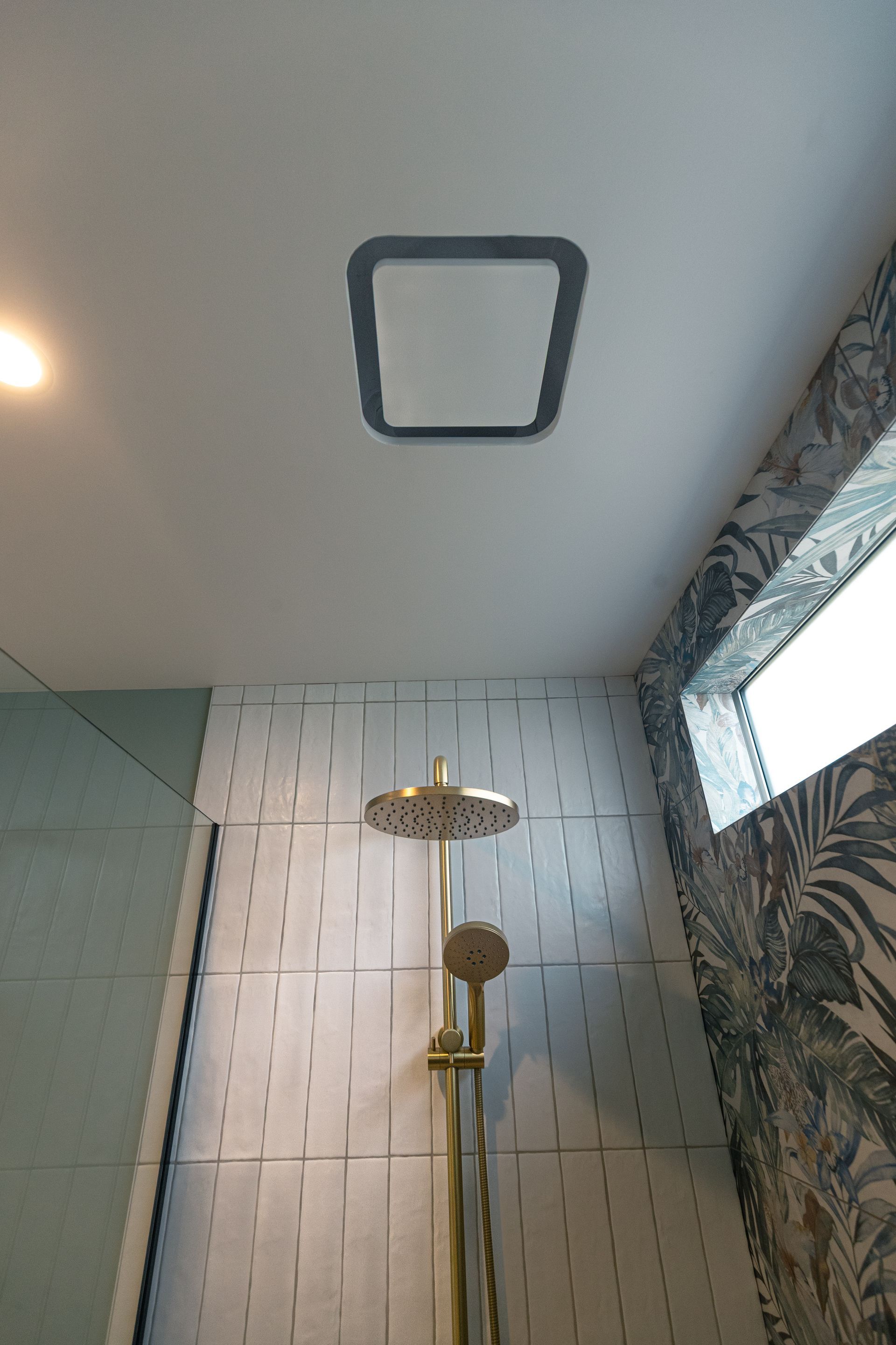 A gold showerhead and handheld attachment mounted against a white textured tile wall in a modern bathroom.