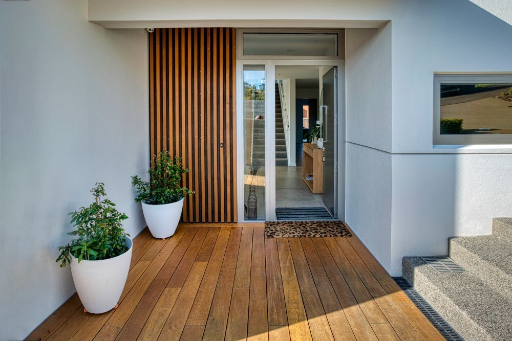 A modern entryway with a wooden deck, two white potted plants, and a glass-paneled door next to vertical wood paneling.