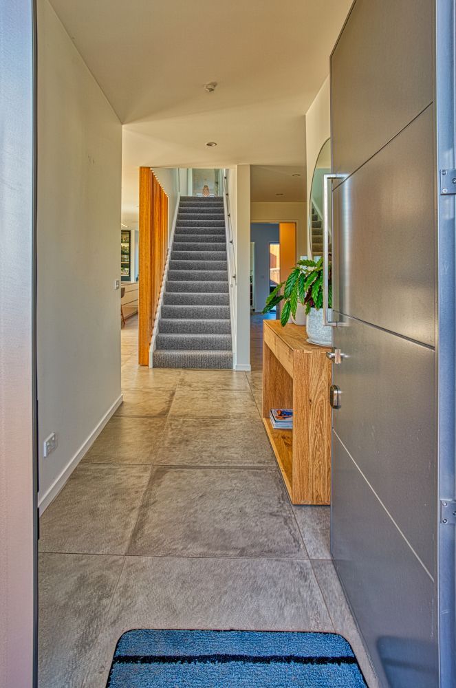 A modern entryway with stone tile floors, a wooden console table with a potted plant, and a carpeted staircase ahead.