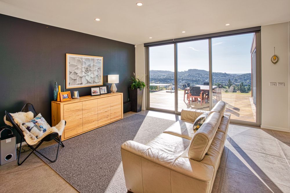 A modern living room with a cream sofa, wood credenza, and butterfly chair against a dark wall, overlooking a patio view.