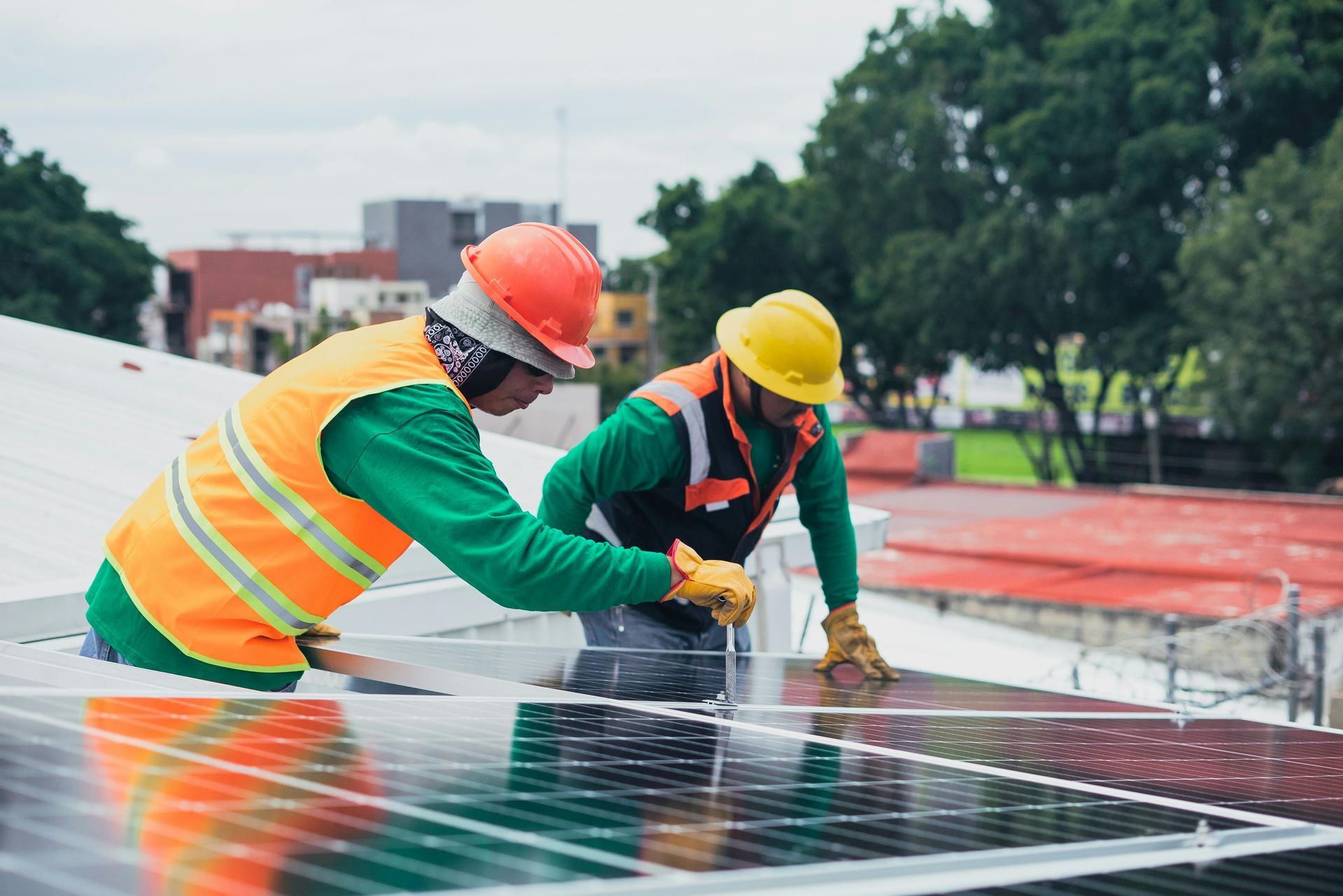 Two workers in hard hats and safety vests install solar panels on a rooftop.