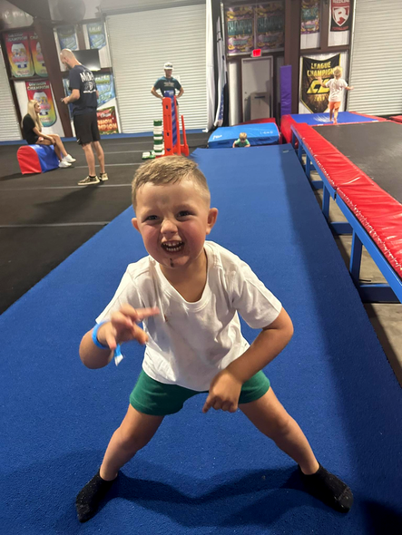 Young boy with a delighted expression poses on blue mat, arms outstretched.