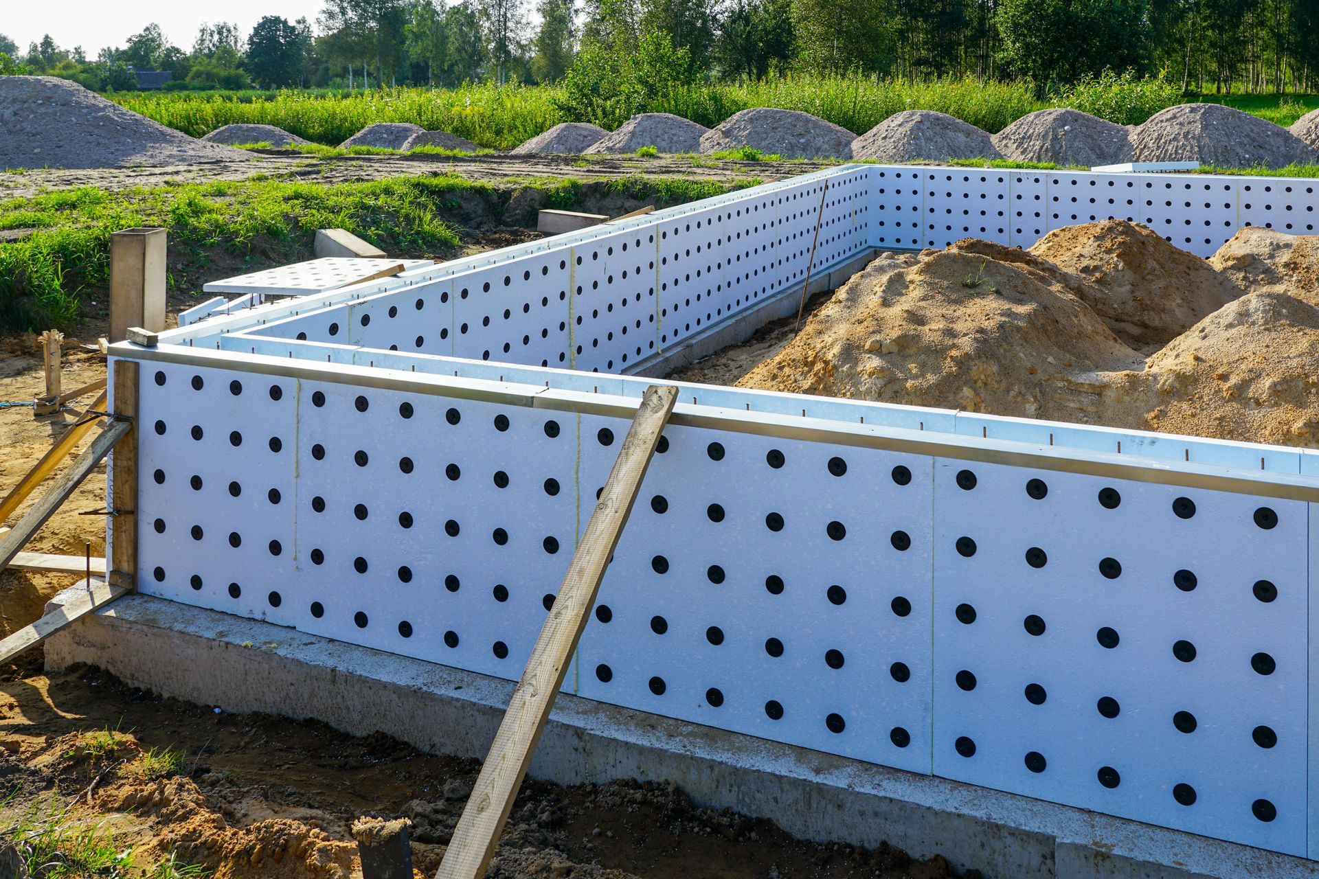 Coffrage de fondation en panneaux poreux blancs avec des tas de terre et de gravier en arrière-plan.