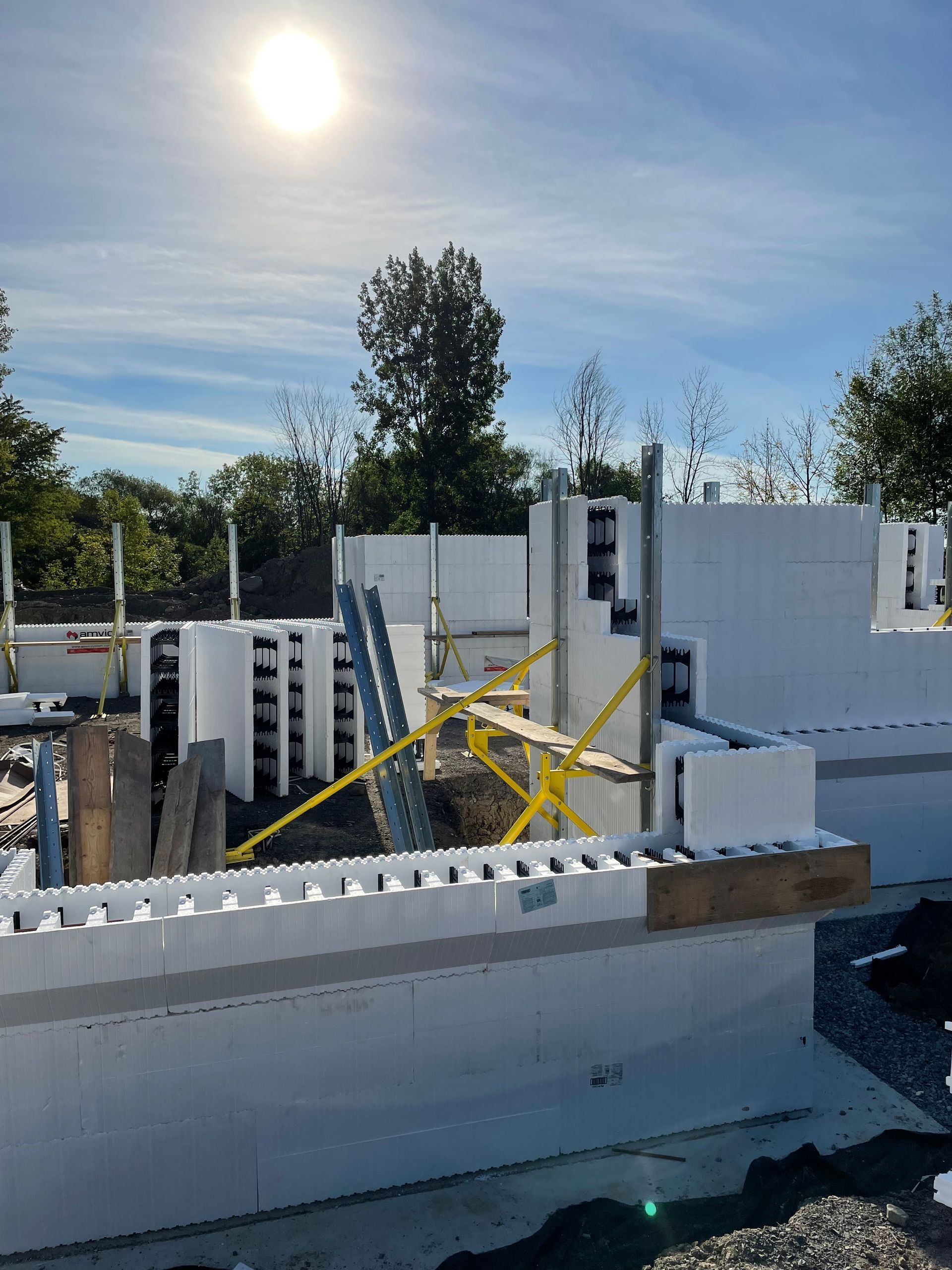 Chantier de construction avec des blocs de mousse blanche formant des murs, échafaudages, journée ensoleillée.