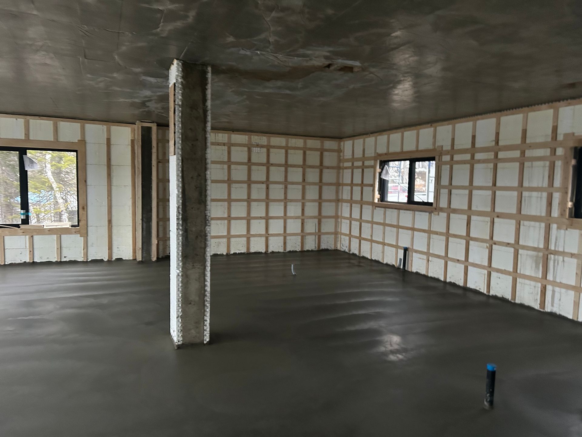 Intérieur d'un bâtiment en construction, montrant un sol en béton et des murs isolés avec une structure en bois.